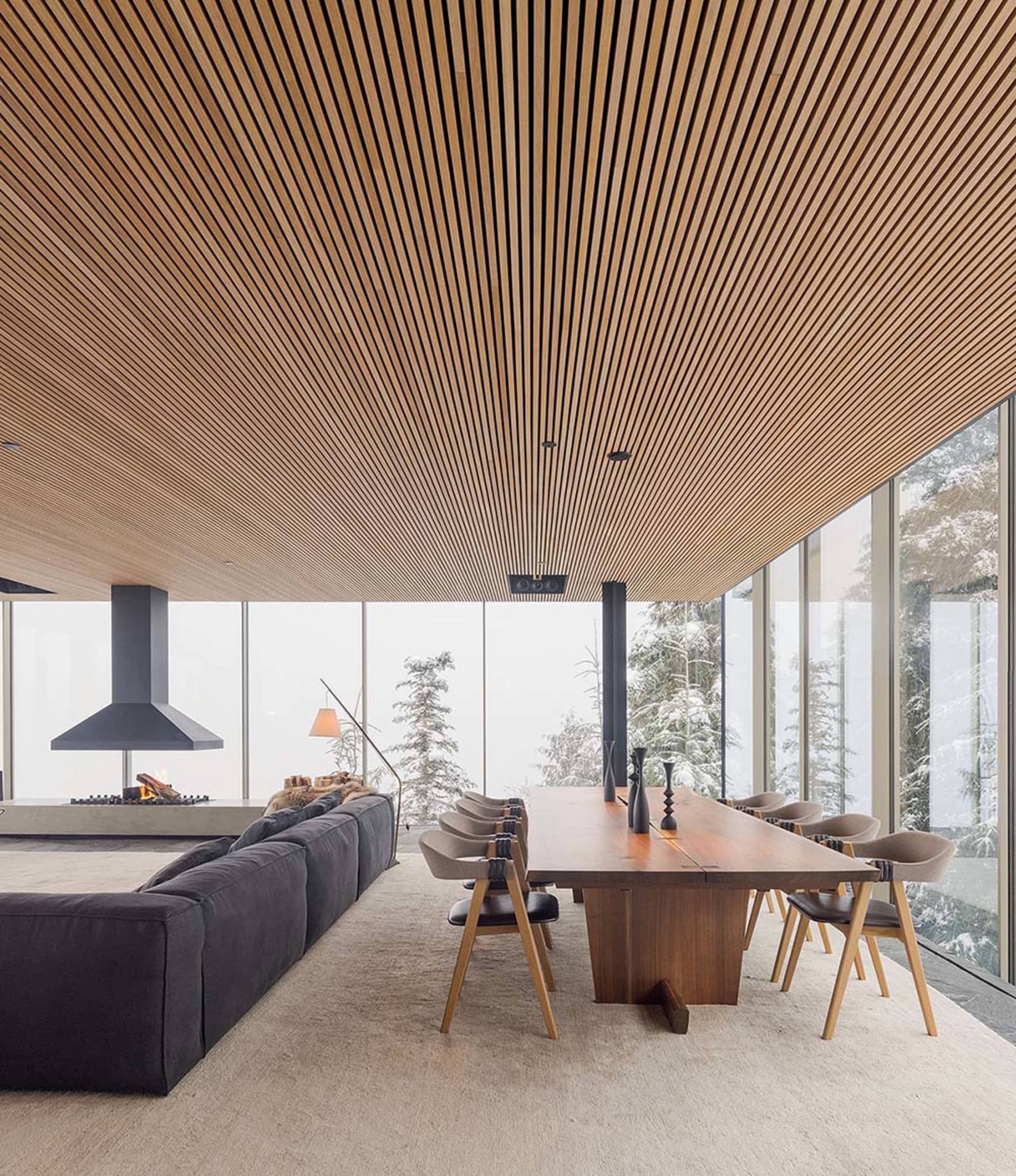 Modern living and dining room with wooden ceiling, glass walls, and carpet floor.