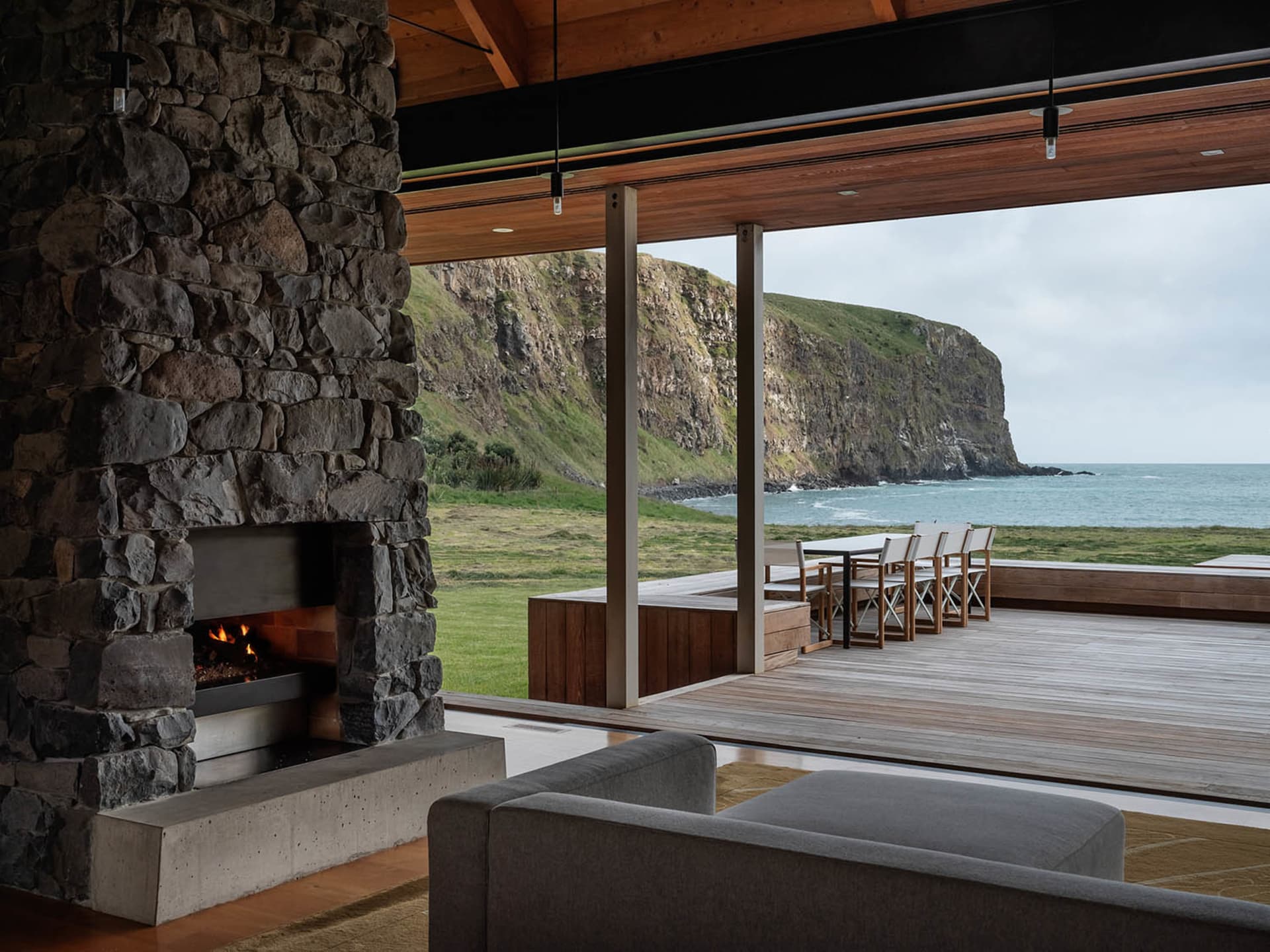 A modern coastal residence featuring a stone fireplace with a living area and outdoor deck overlooking the ocean.