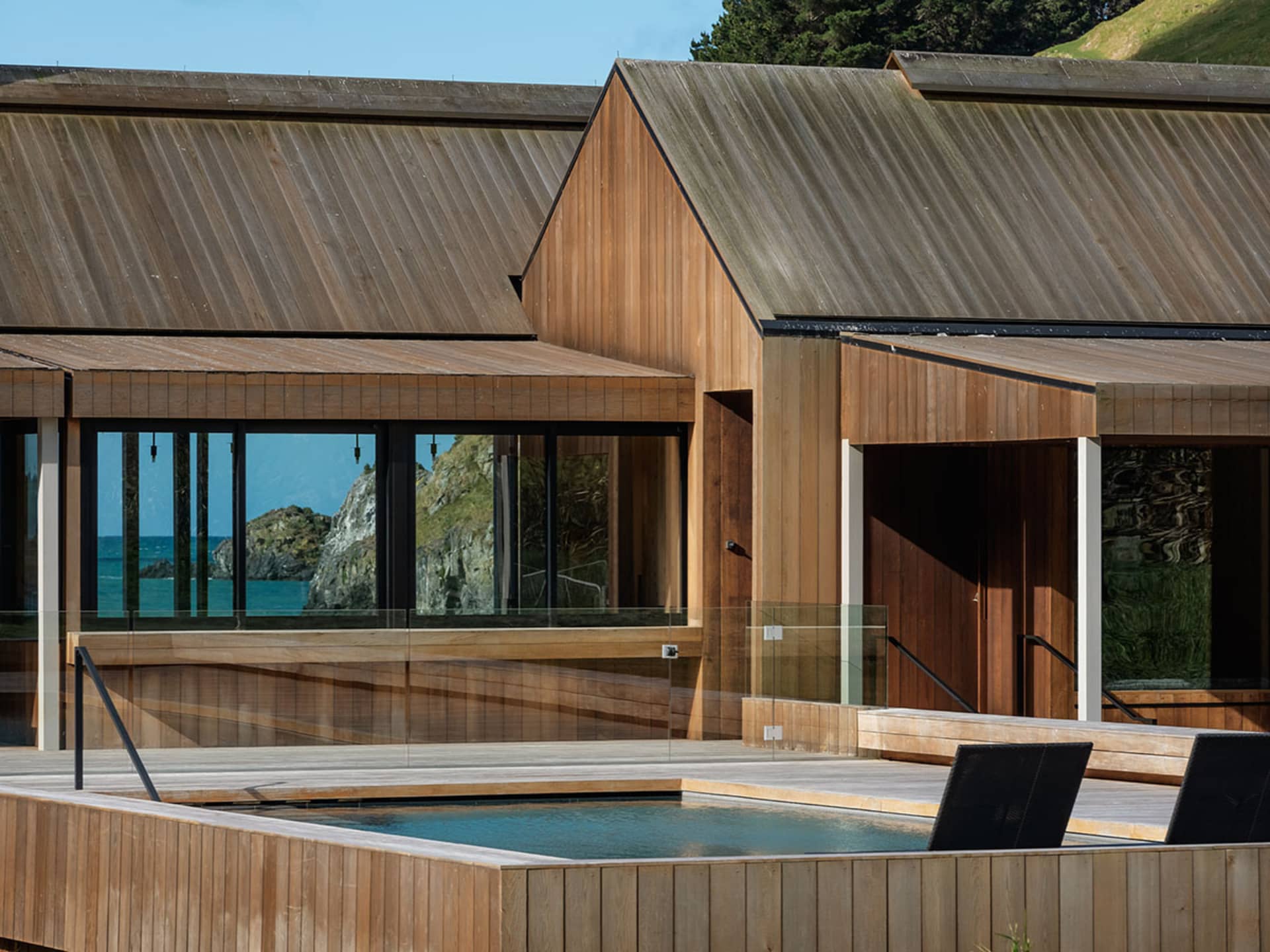 A modern residential exterior with wooden siding and a rooftop terrasse overlooking the ocean.