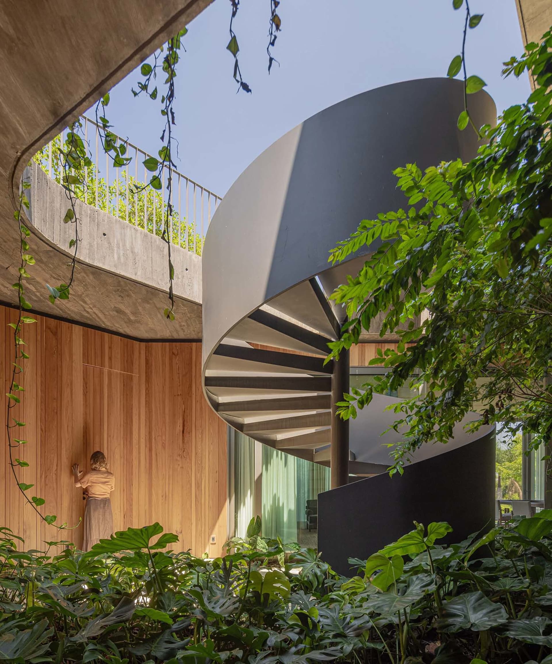 A modern interior featuring a metal spiral staircase surrounded by lush greenery.