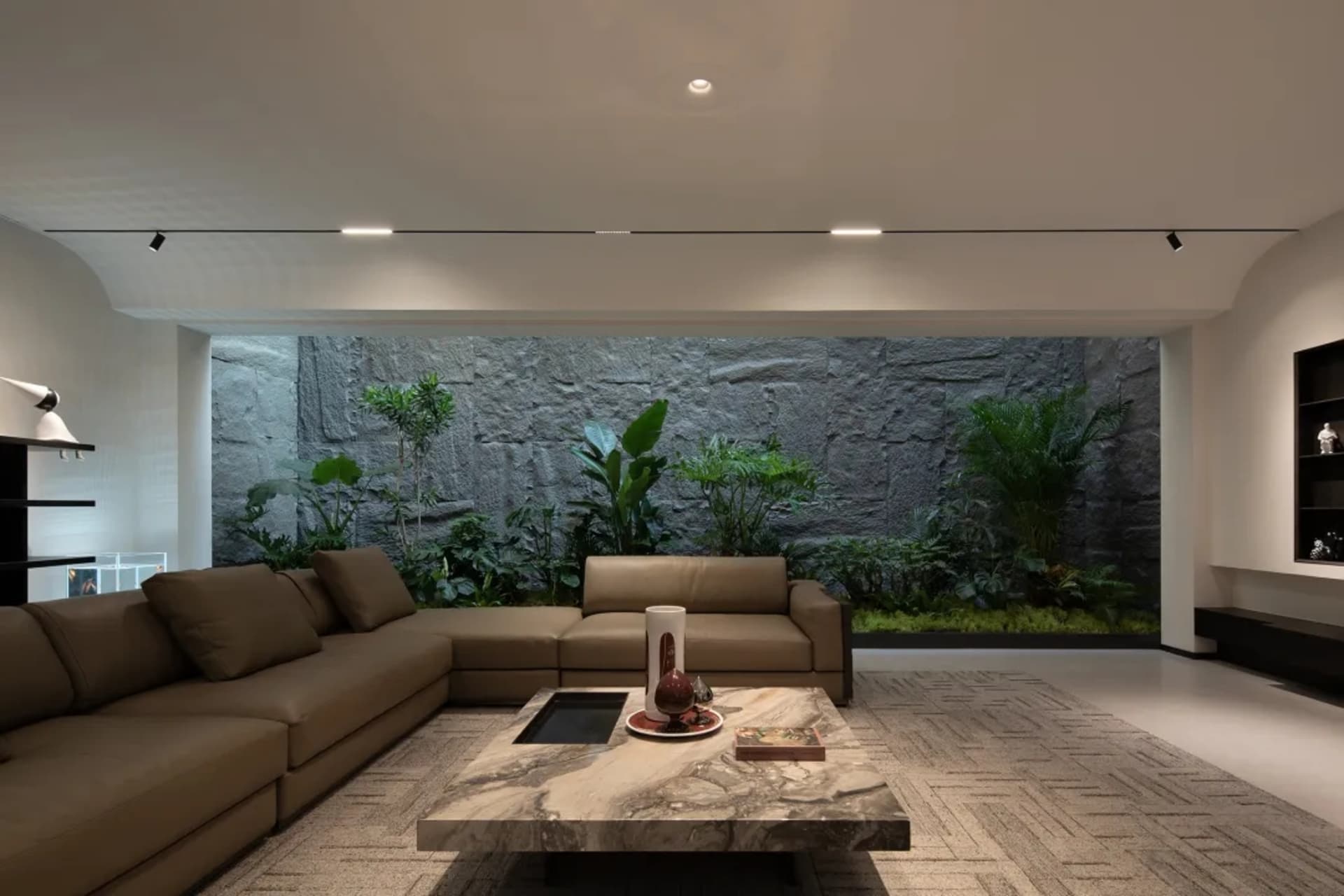Modern living room featuring a beige leather sectional sofa in front of a stone wall with plants and greenery.