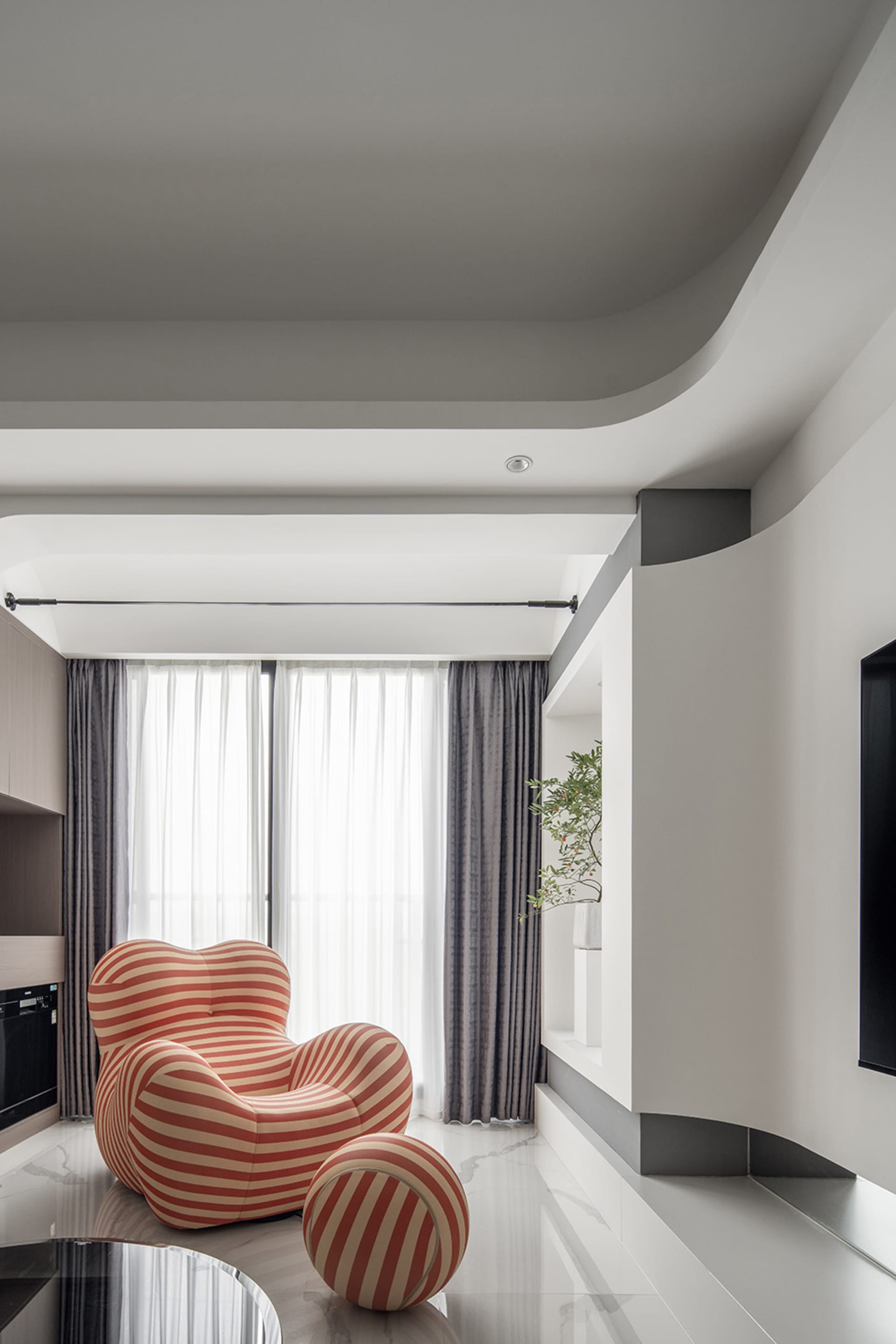A modern living room with a striped armchair and ottoman, featuring glass and fabric materials.