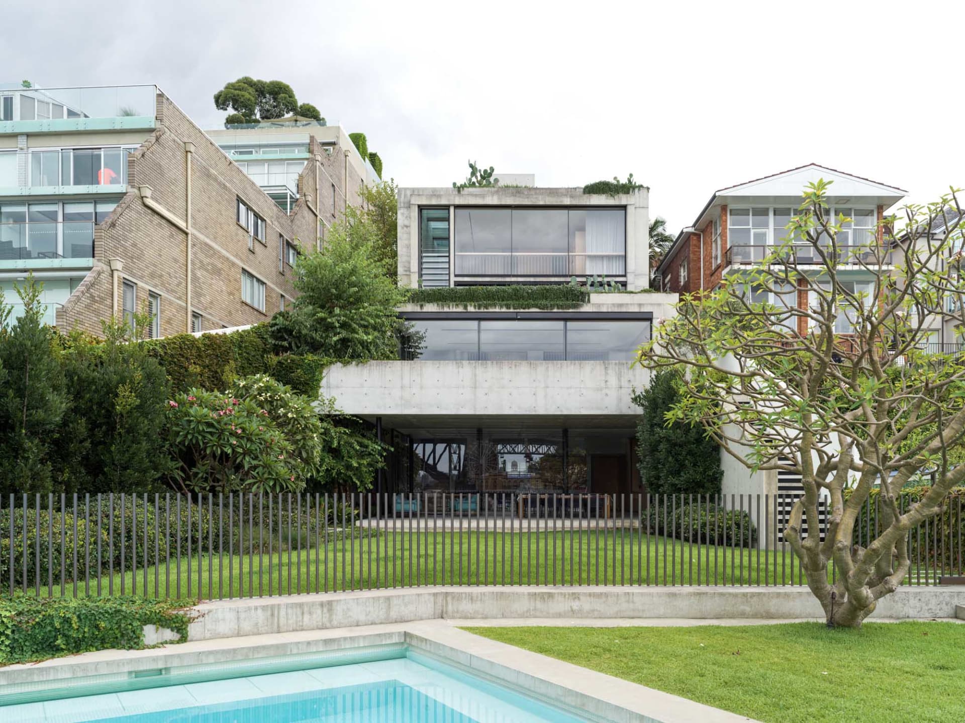 A modern residential home exterior showcasing a concrete facade with large glass windows and a rooftop garden.