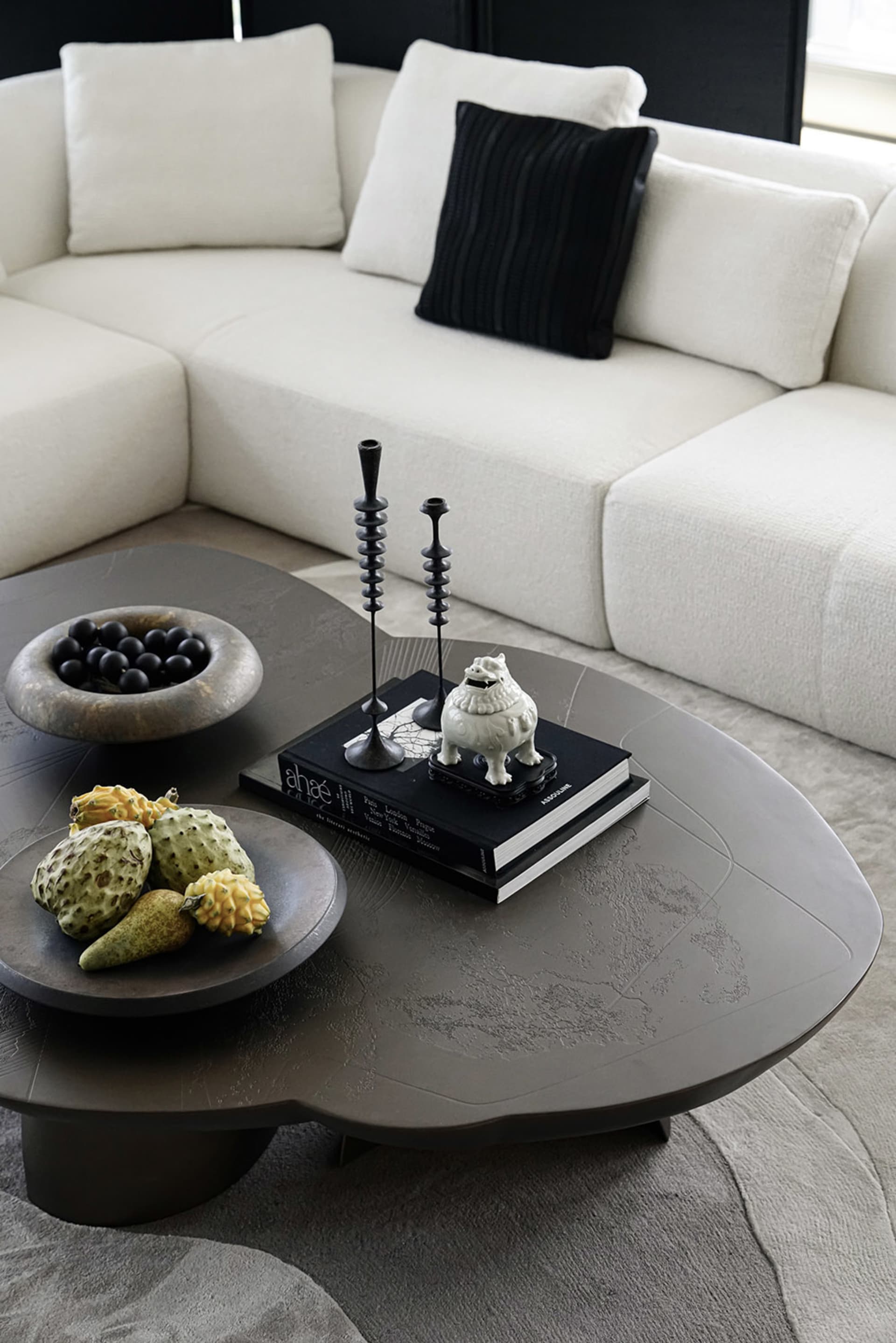 A modern living room with a large sectional sofa, a unique concrete coffee table, and decorative elements such as a fruit bow