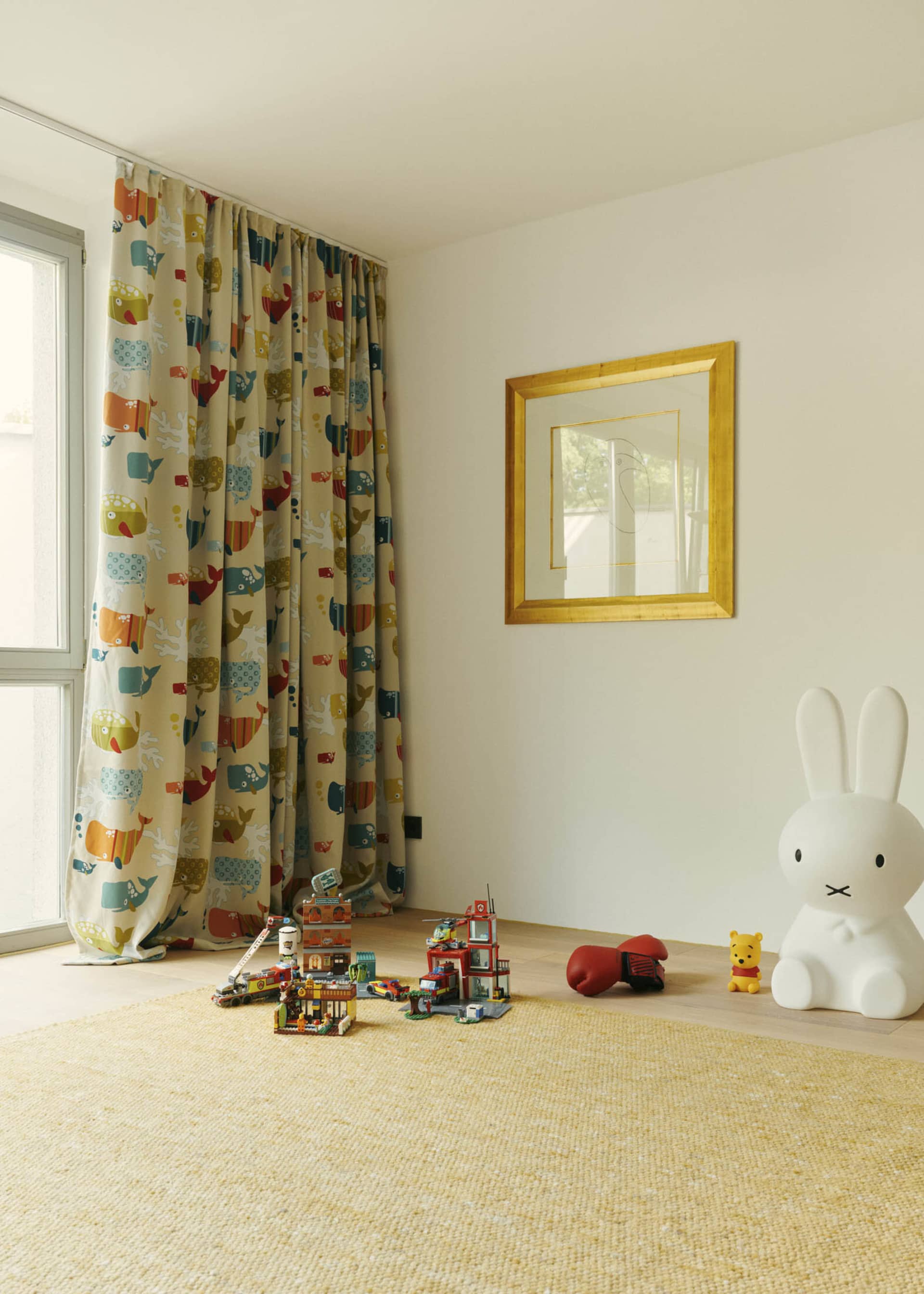 A children's room with playful decor, including colorful curtains, toys, and a large rabbit sculpture.