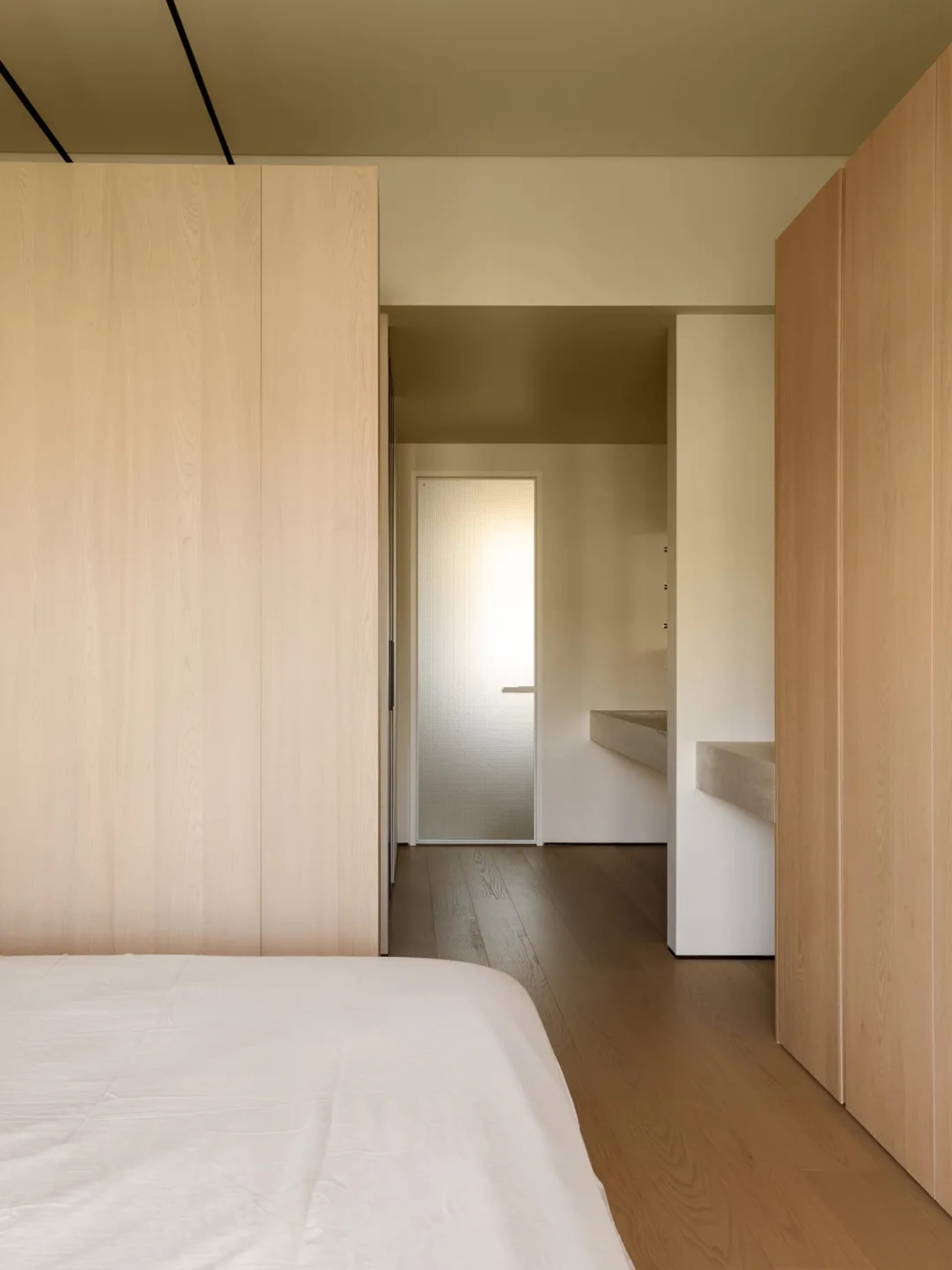 Modern bedroom with wood paneled walls and a white bed.