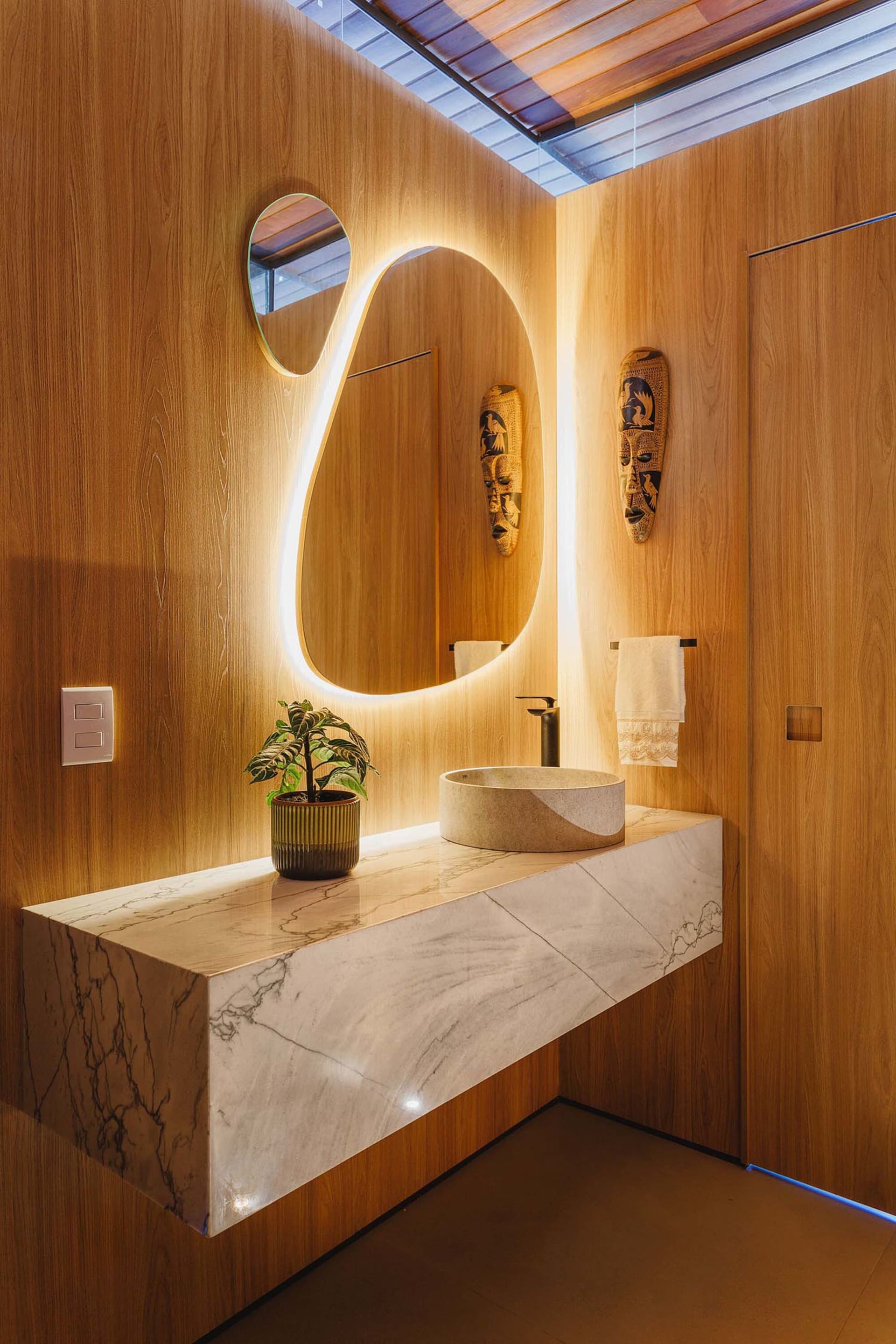 A modern bathroom with a marble countertop, a sink, a mirror with backlighting, and wooden walls.