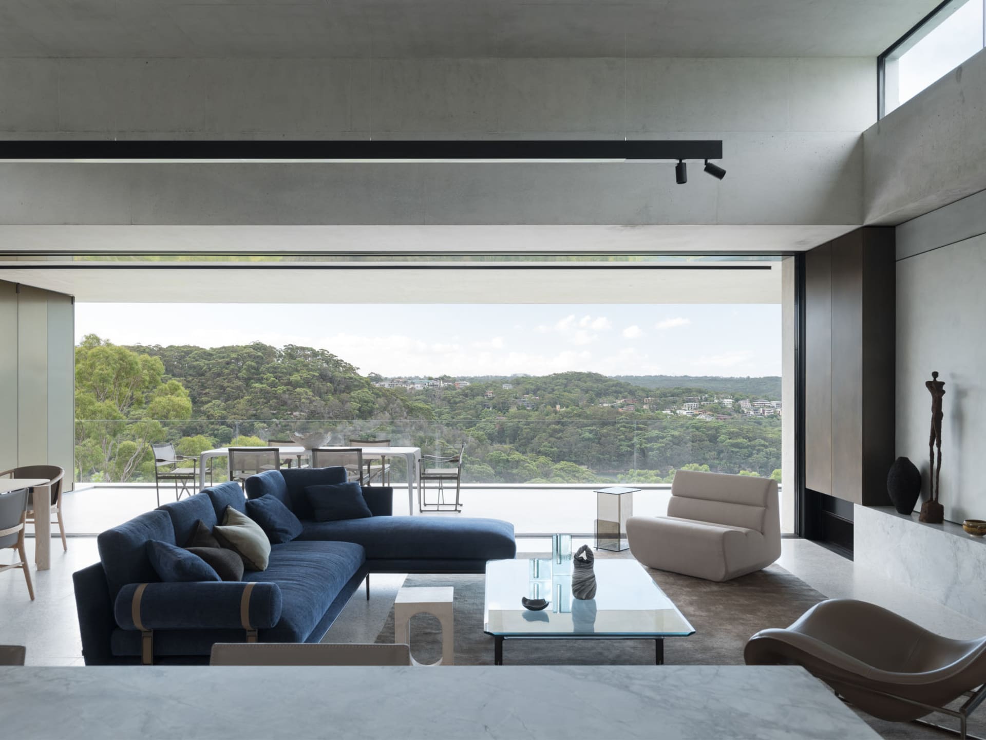 Modern living room with concrete walls and floors, featuring a spacious blue sofa and a glass coffee table.