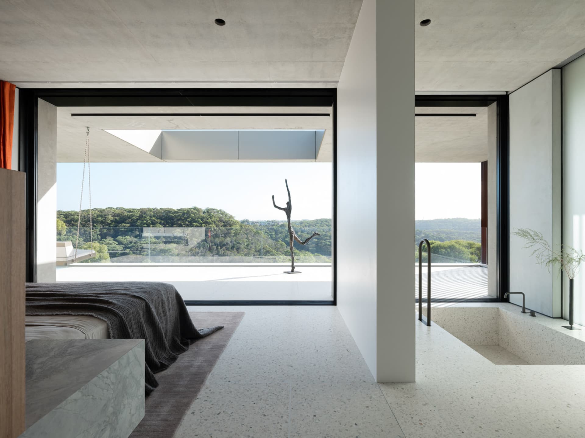 Modern bedroom featuring concrete flooring and walls, with a view of trees outside through large windows.