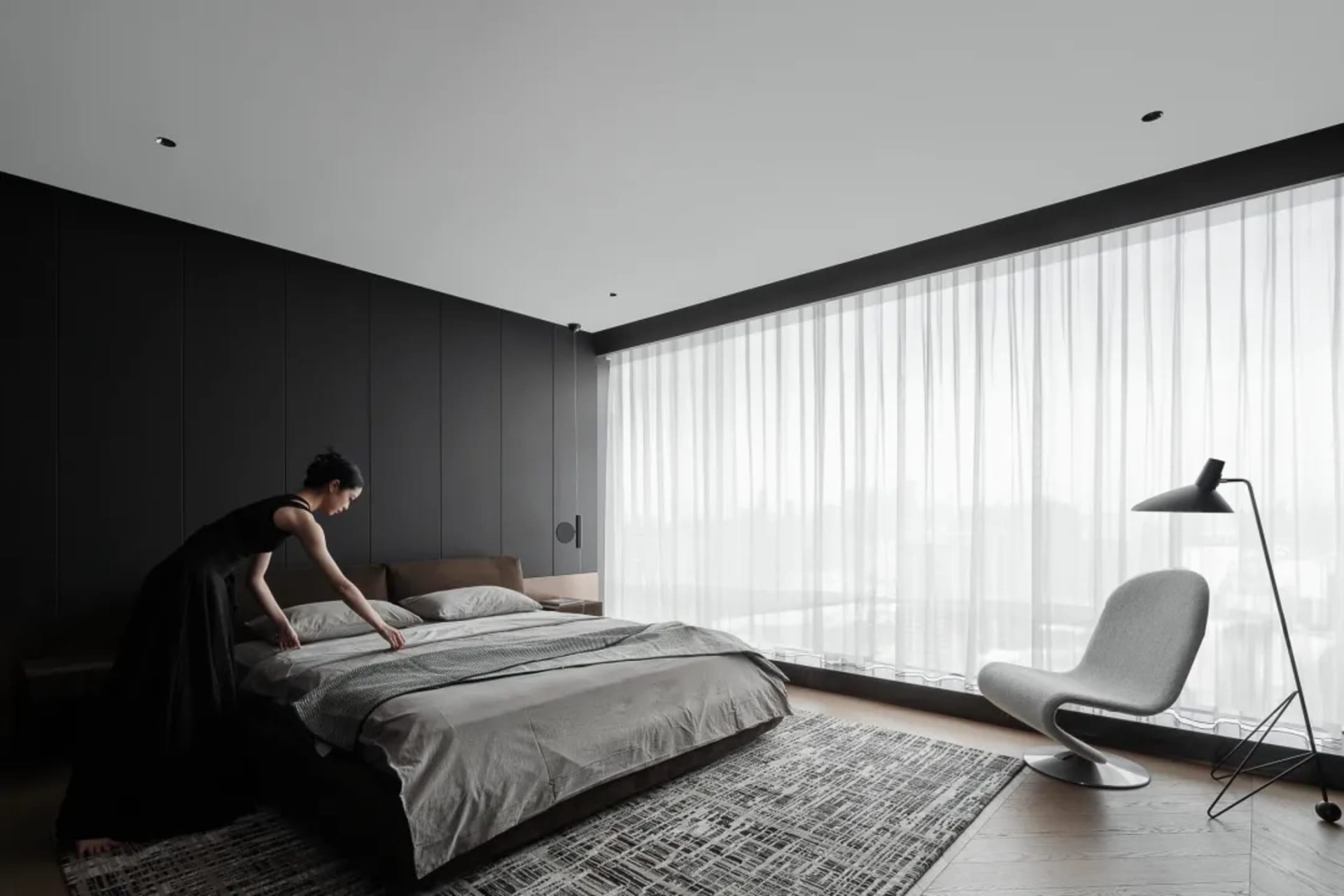 A modern minimalist bedroom featuring a bed with textured brown sheets and pillows, a gray armchair, and a floor lamp.