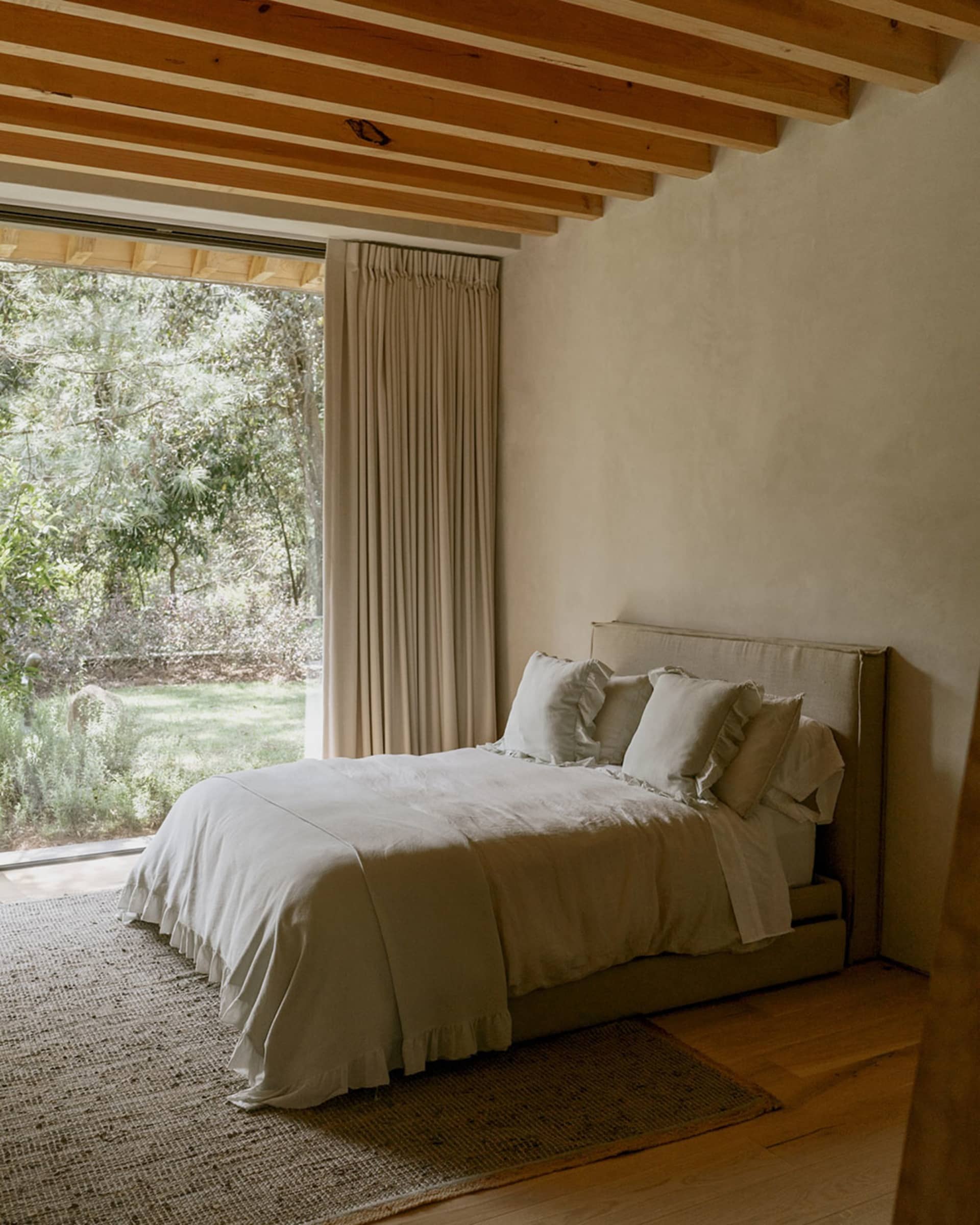 A minimalist bedroom featuring a bed with white bedding and neutral-toned walls and ceiling