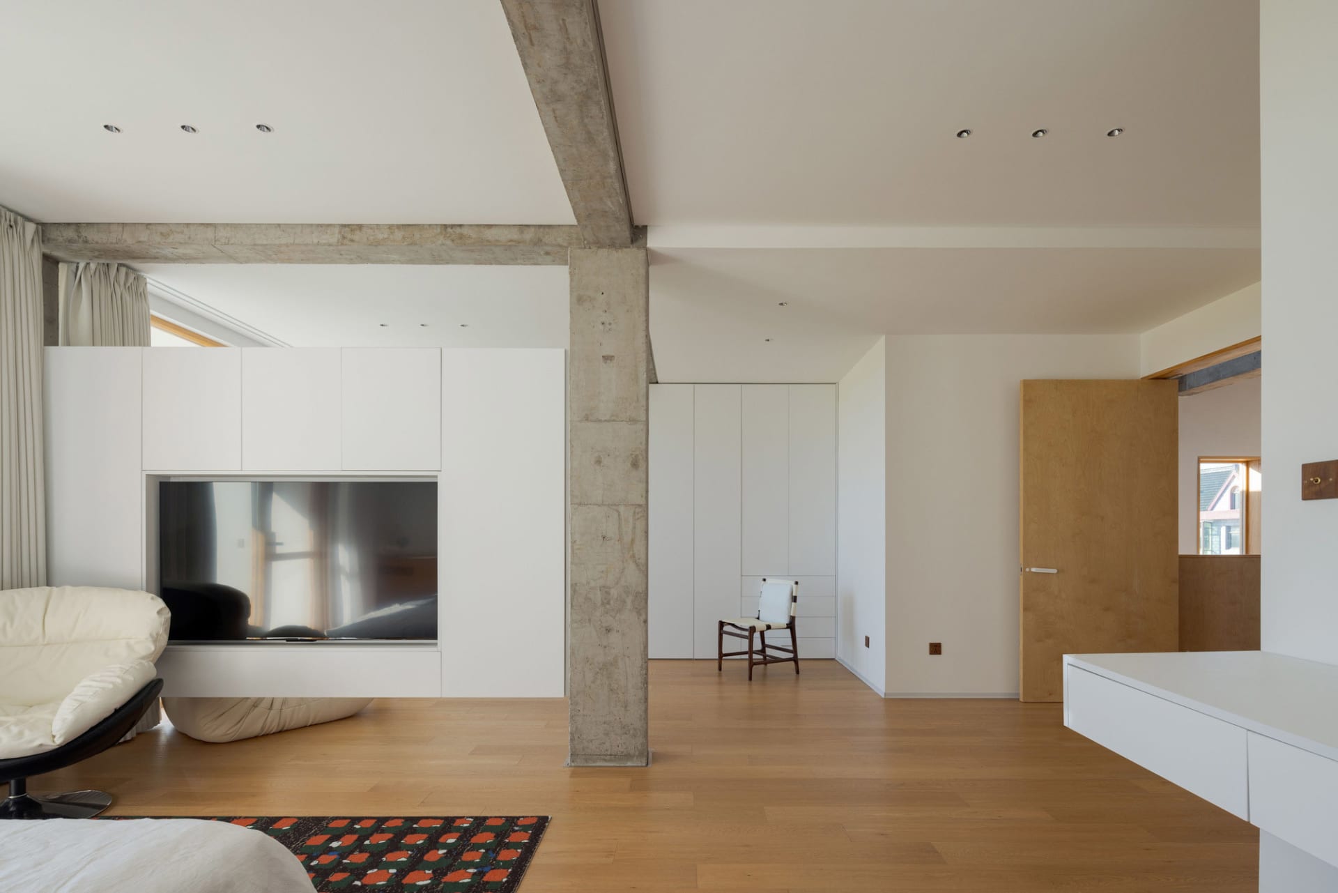 Modern living room with a concrete fireplace, white furniture, and a rug on wooden floor.