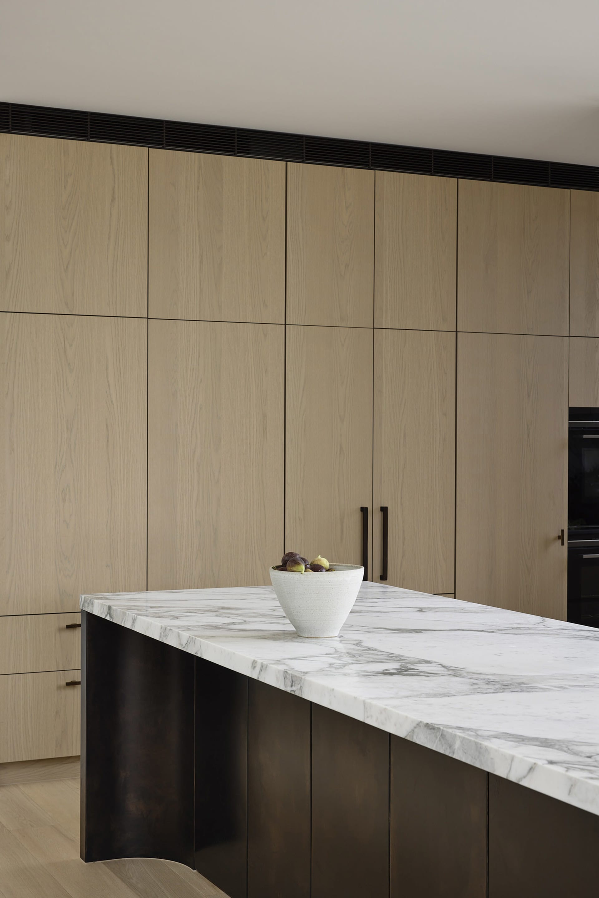 A modern minimalist kitchen featuring a marble countertop with a bowl of fresh figs.