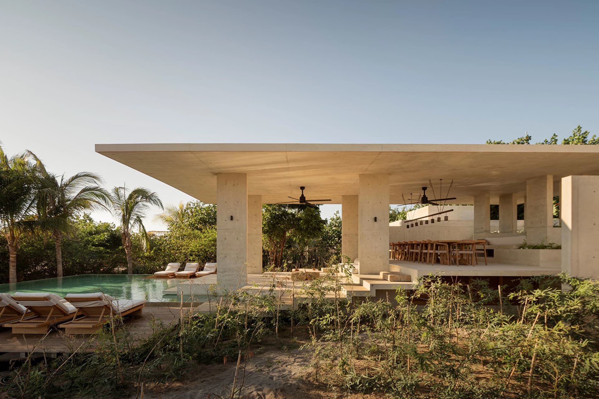 A modern residential structure with a concrete exterior and a large outdoor area featuring a pool and lounge chairs.