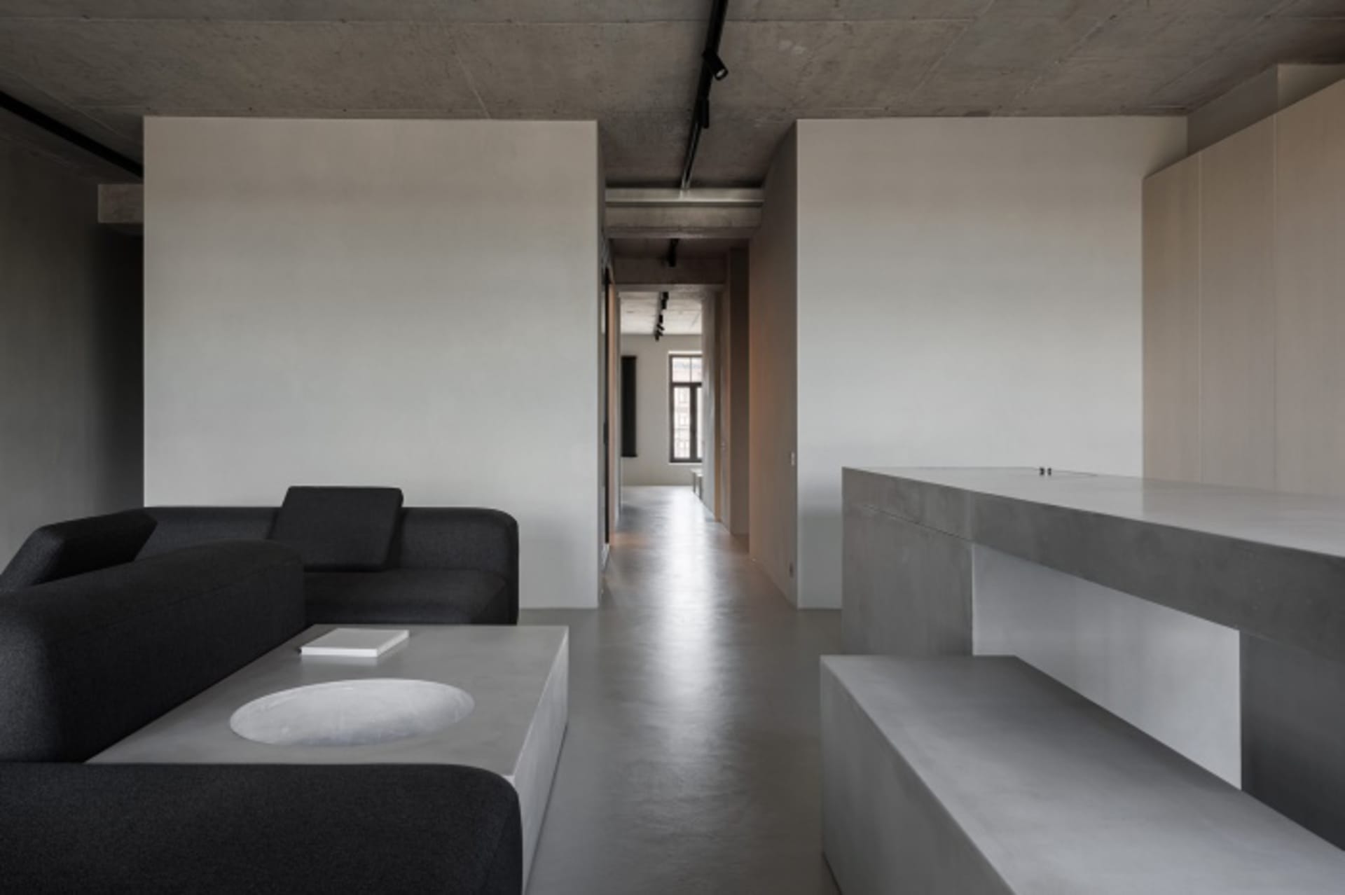 Modern minimalist living room featuring a dark gray sofa, a white coffee table, and a concrete wall and floor.
