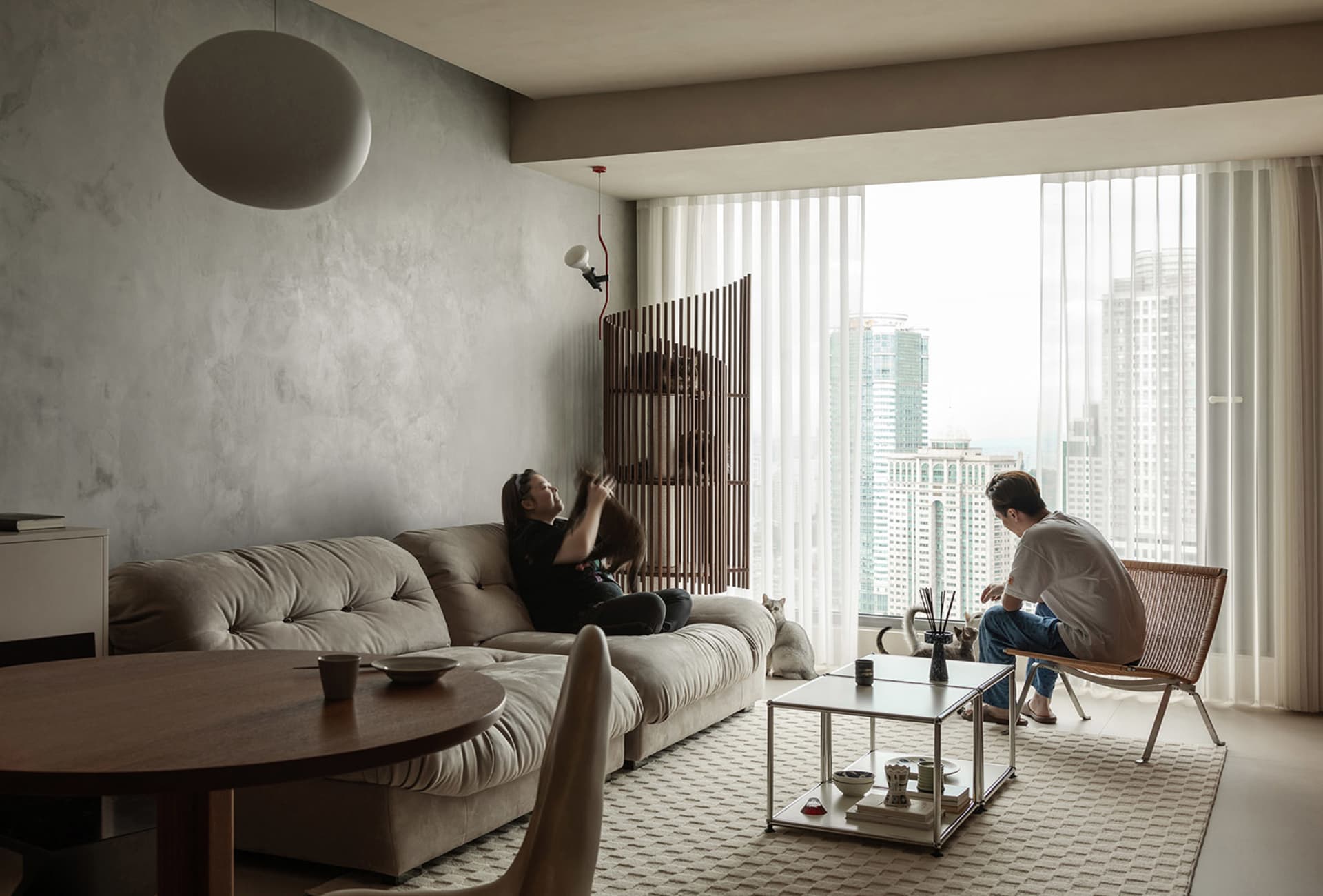 A modern living room with a concrete sofa, wooden coffee table, and large windows overlooking a cityscape.