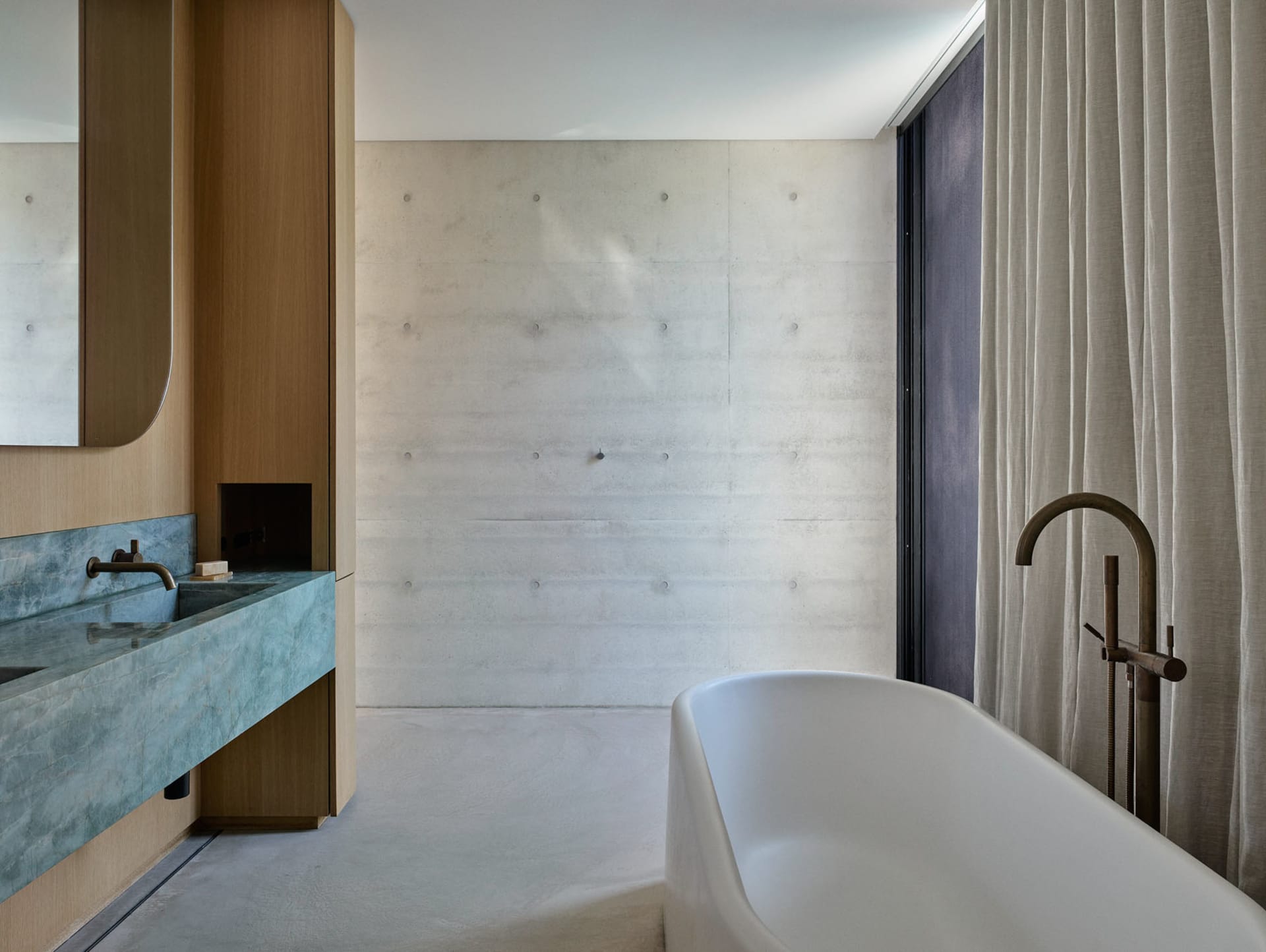 A modern, industrial-style bathroom featuring a concrete wall and floor, minimalist design, and freestanding bathtub.