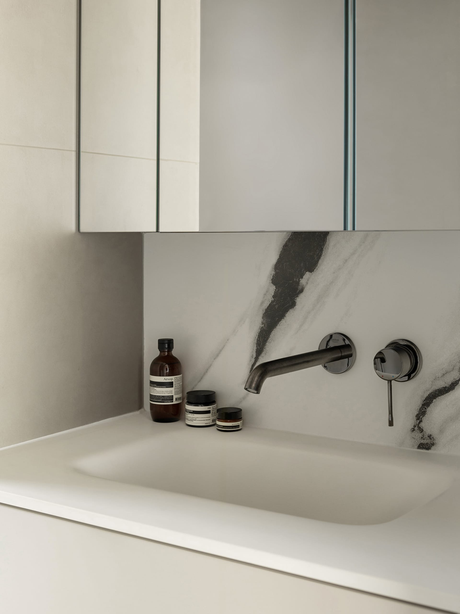 A modern bathroom featuring a white marble countertop and sink, minimalist design, and sleek, dark fixtures.