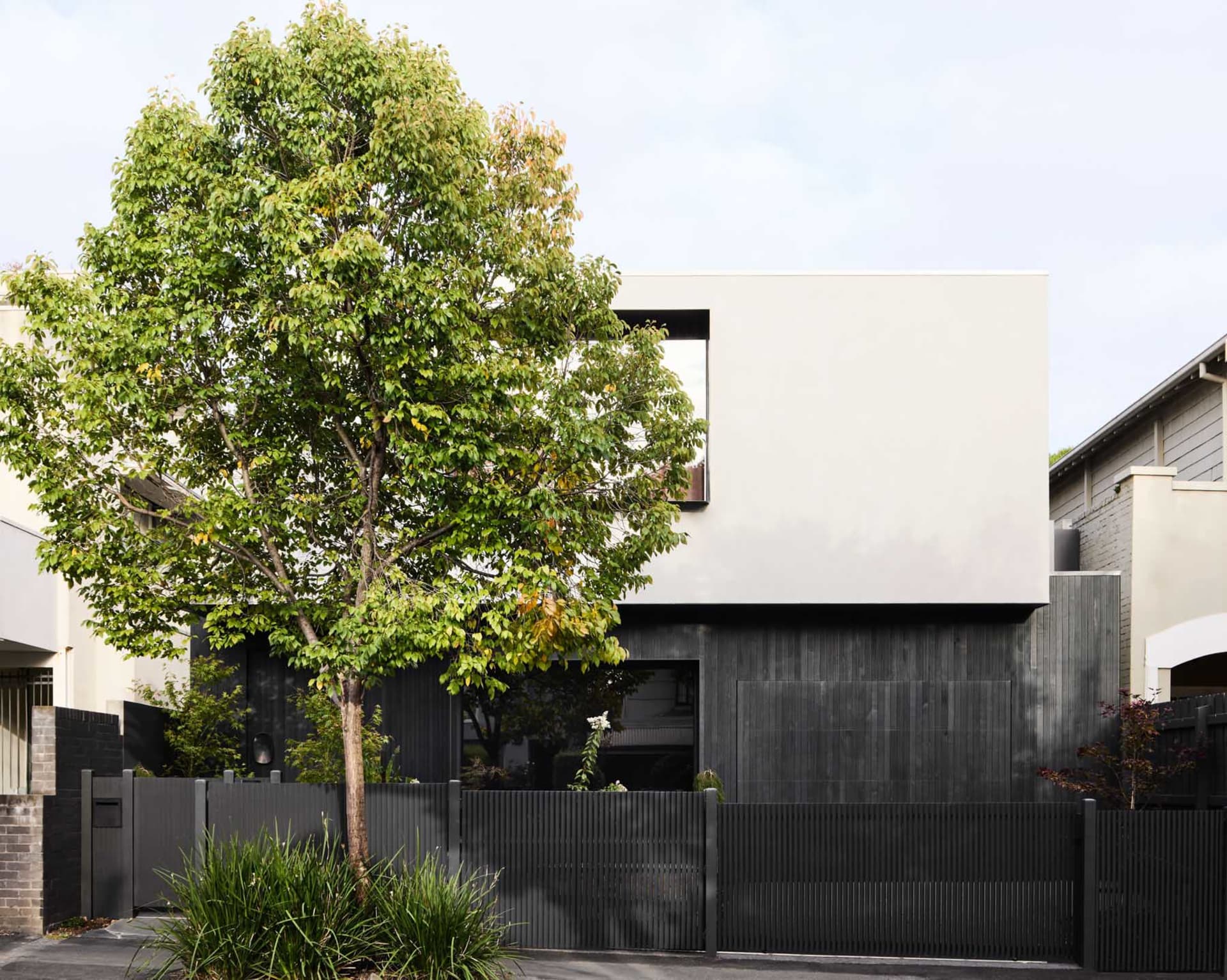 A modern residential home with white concrete exterior and black wooden accents.