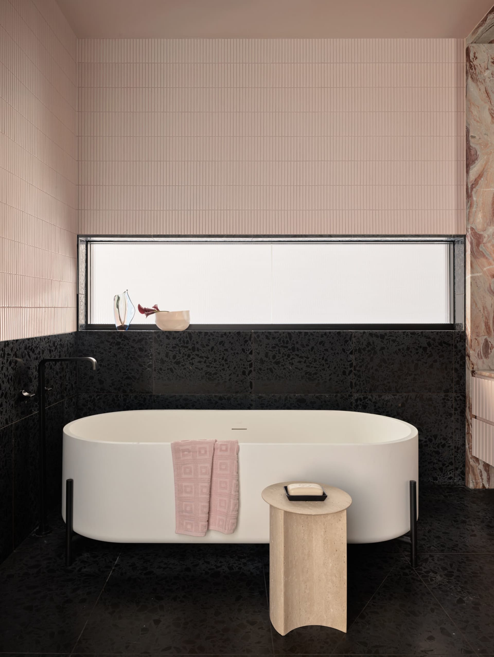Contemporary bathroom featuring a freestanding tub, pink hand towel, and black terrazzo tiles.