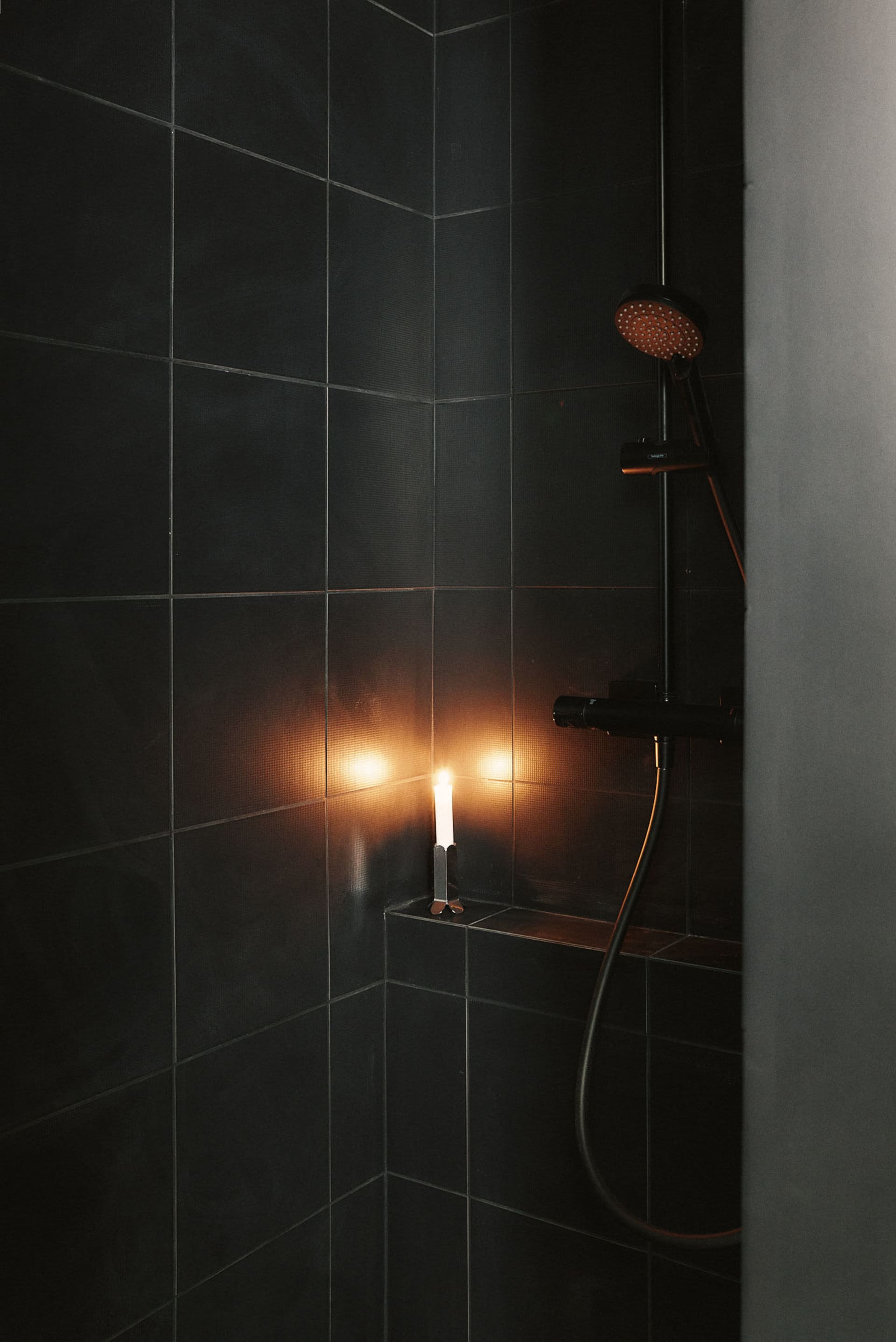 A minimalist bathroom with black tiles and a glowing candle.