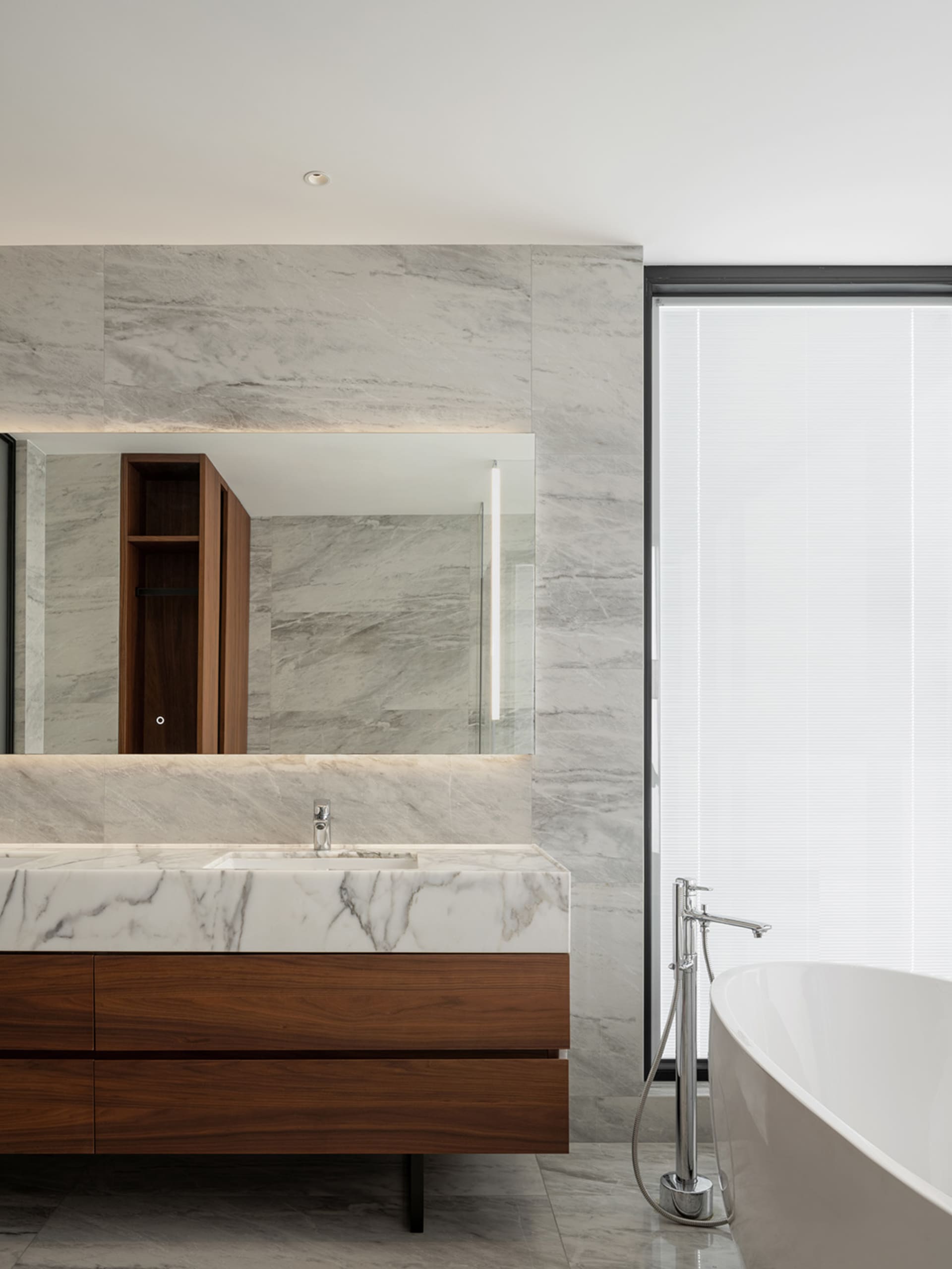 Modern bathroom featuring marble countertop and wood vanity with a freestanding bathtub and large window.