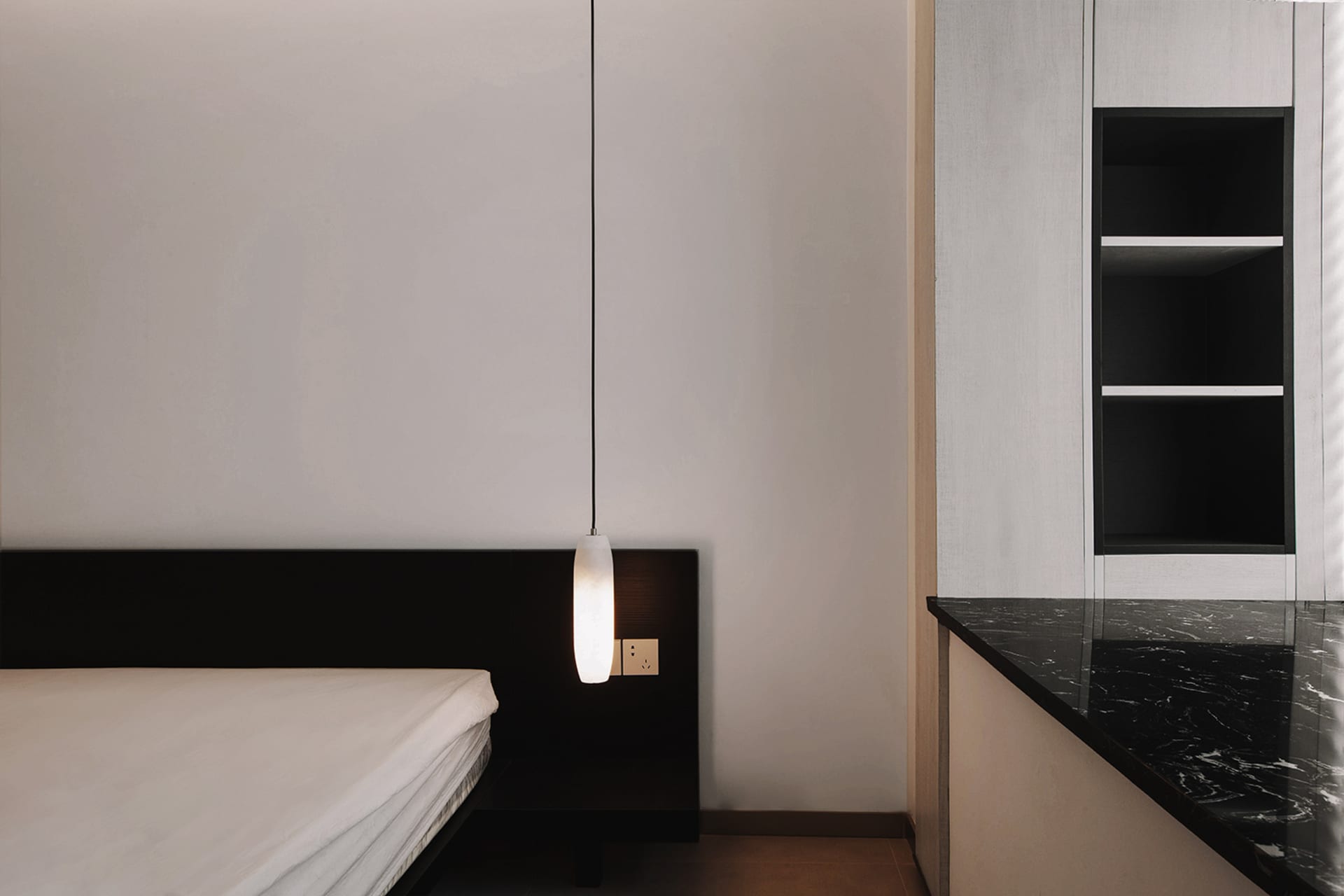 A minimalist bedroom featuring a bed with a simple black headboard, a sleek black light fixture, and a marble countertop.
