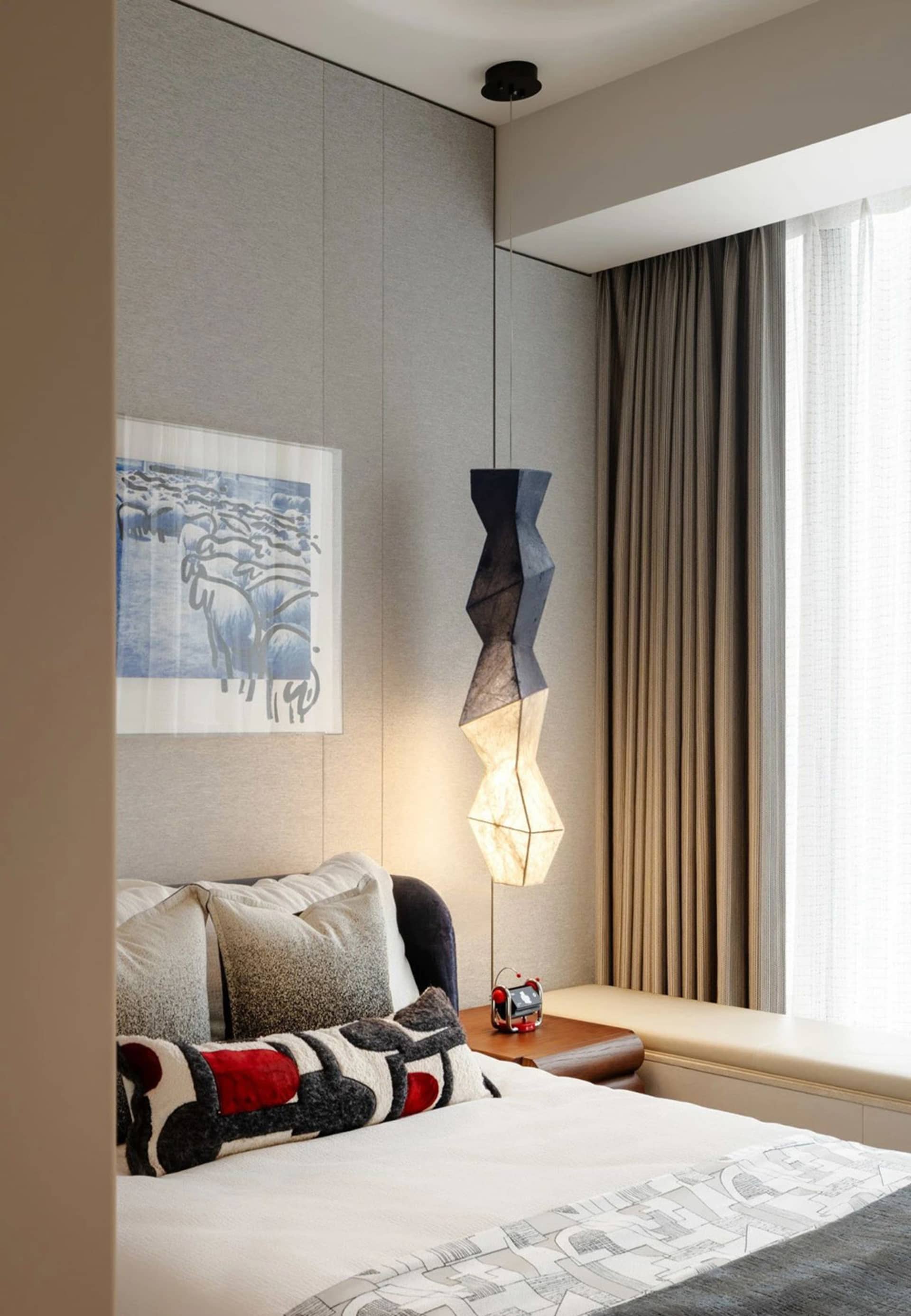 A modern bedroom with a fabric lamp hanging above the bed, surrounded by curtains and pillows.