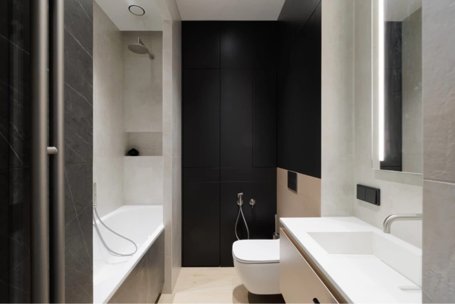 A modern bathroom with white ceramic tiles and black accents, featuring a white bathtub, white toilet, and white sink with a 