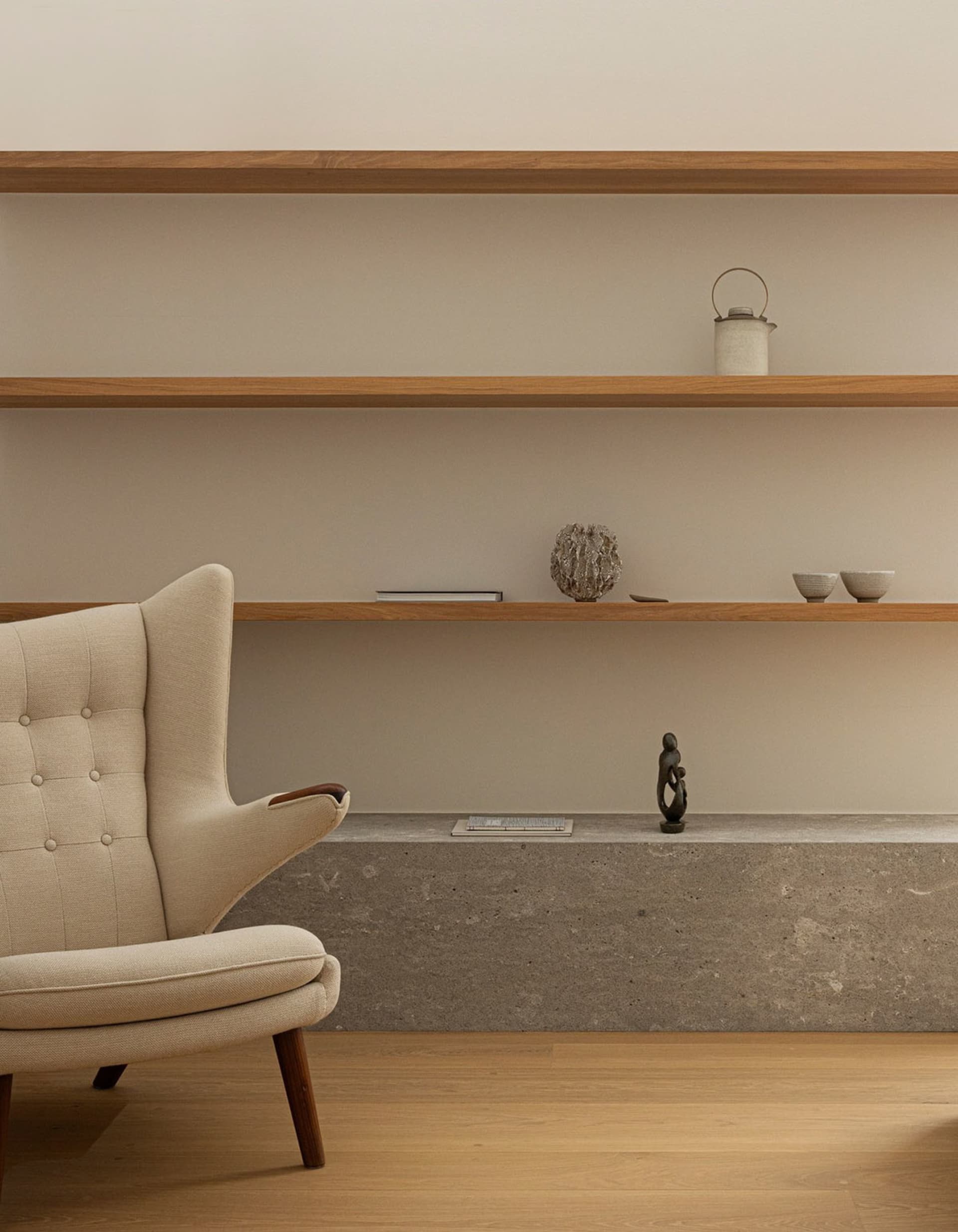 A minimalist living room with wooden concrete shelves, a beige upholstered armchair, and decorative objects.
