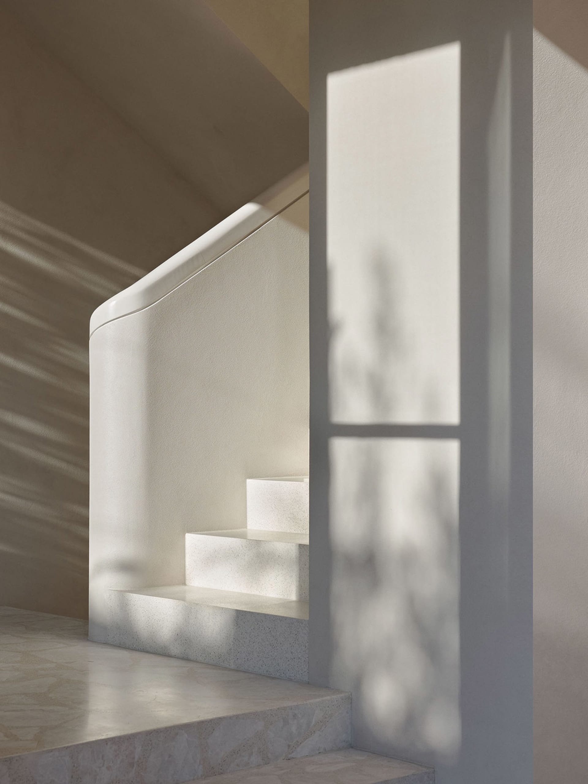 Modern staircase with marble steps and concrete wall, featuring light filtering through a window.