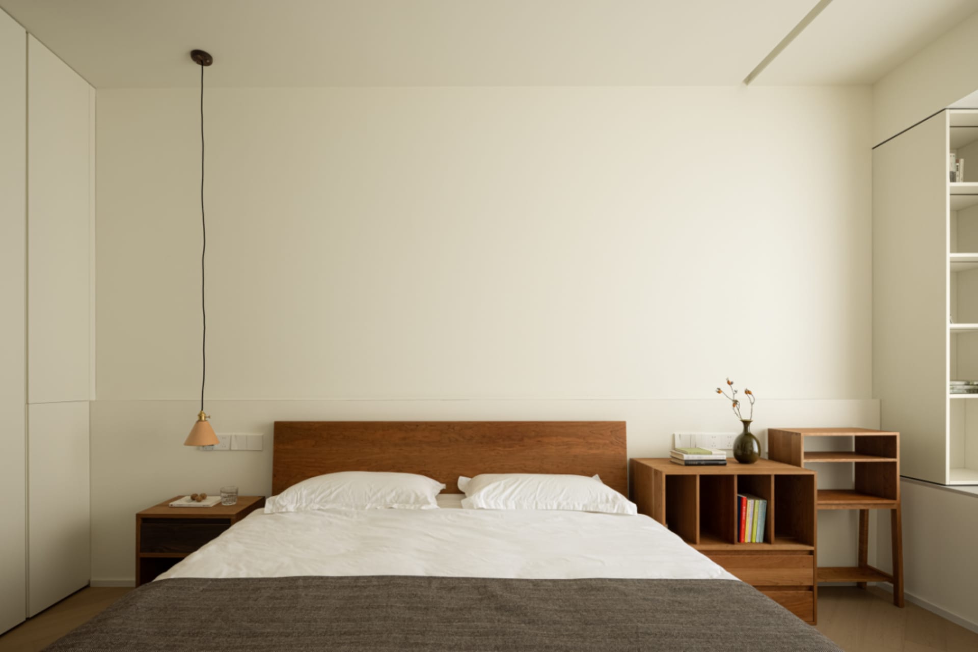 A minimalist bedroom featuring a wooden bed with white bedding and a pendant light hanging from the ceiling.