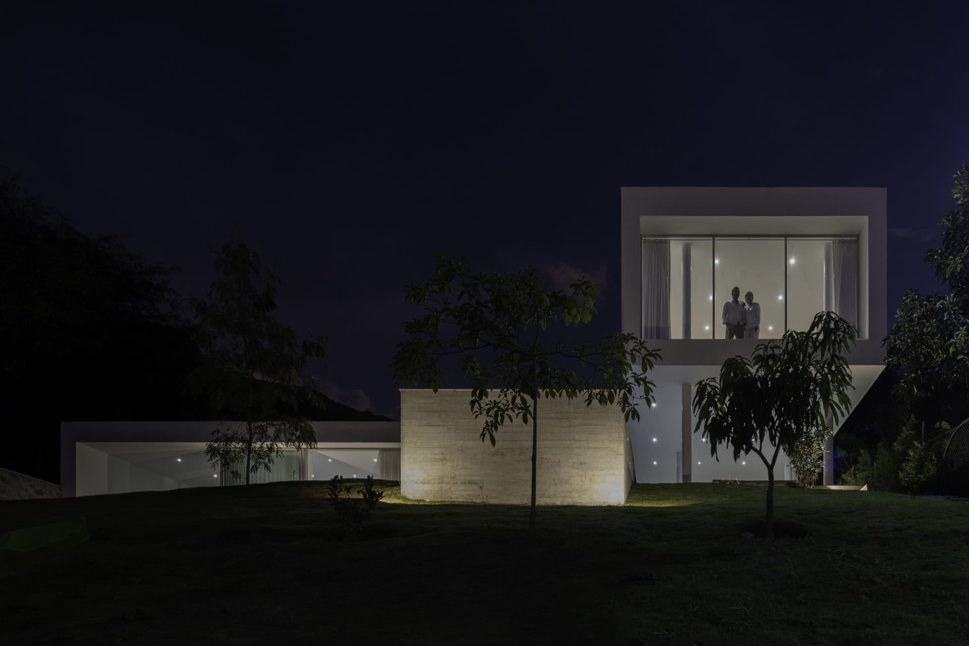 夜晚的現代住宅建築，外牆為混凝土材質並搭配大型窗戶。