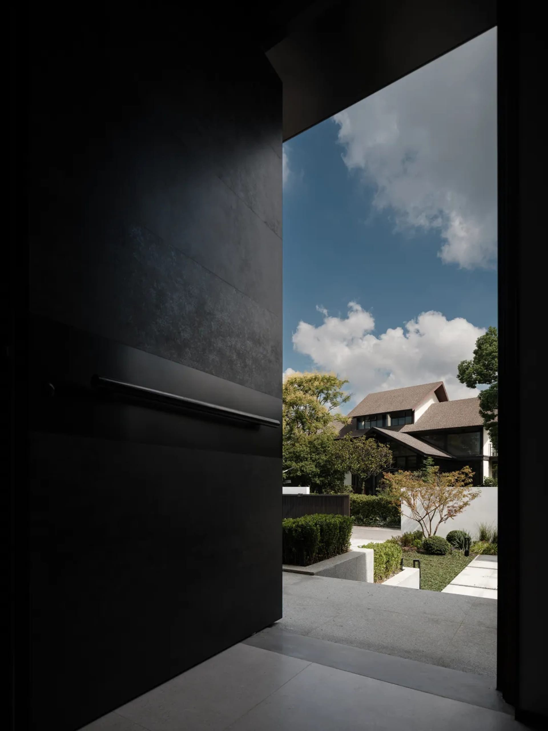 Modern residential house exterior made of concrete with greenery, clear blue sky and clouds above.