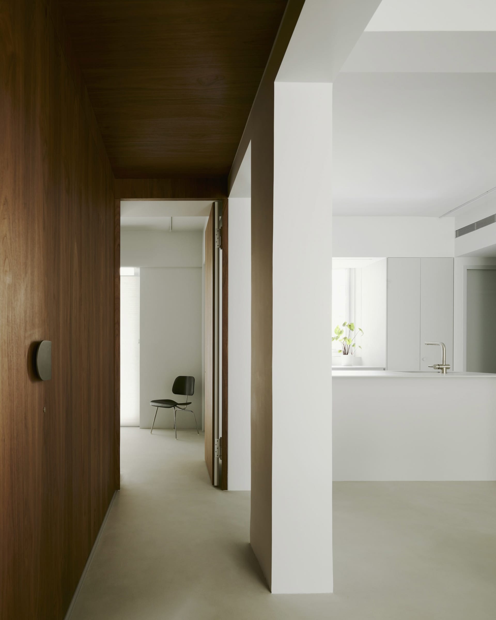 Minimalist living room with concrete floor and walls, featuring a single black chair in the background.