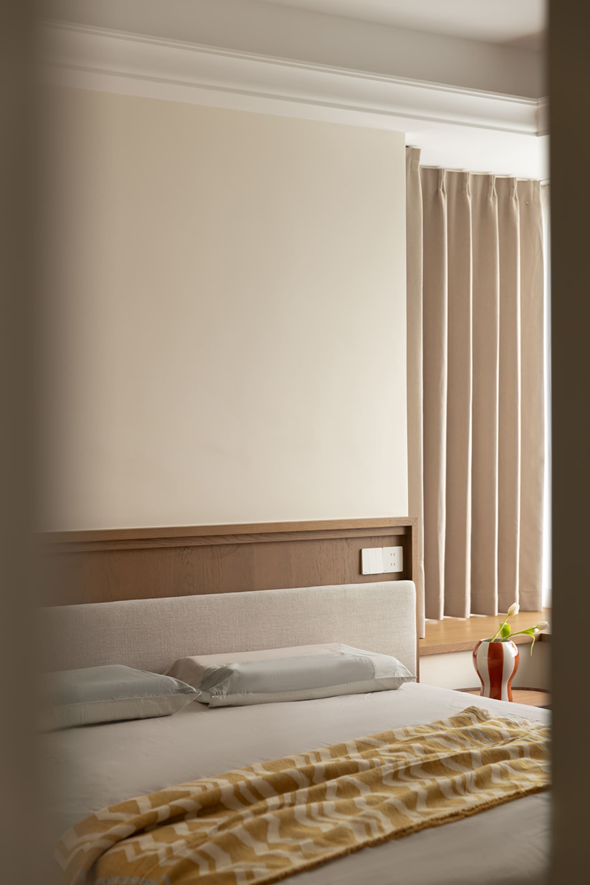 Minimalist bedroom with a bed featuring a fabric blanket, white bedding, and a wooden headboard.