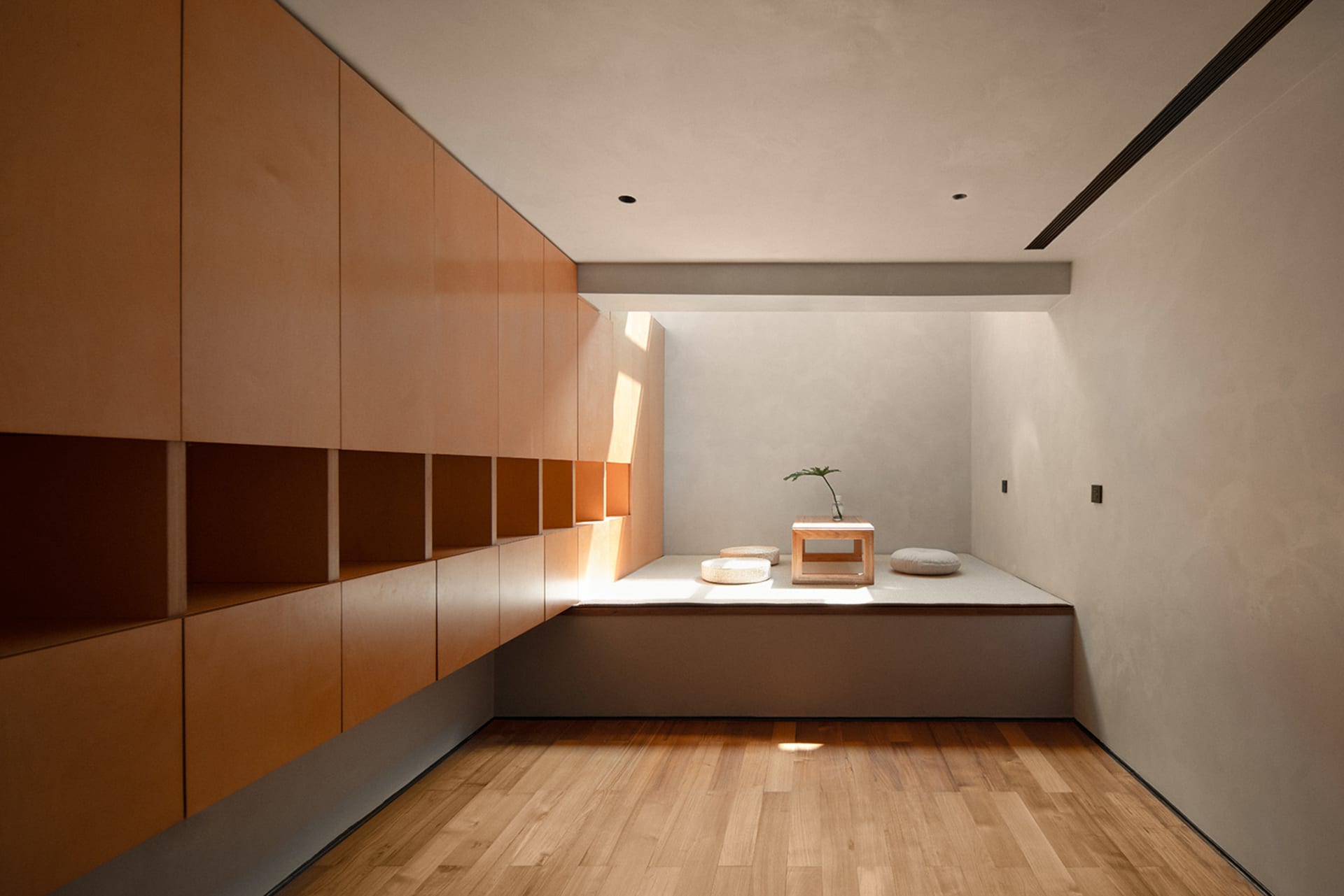 Minimalist living room with wooden furniture and floor, featuring a low table and cushions.