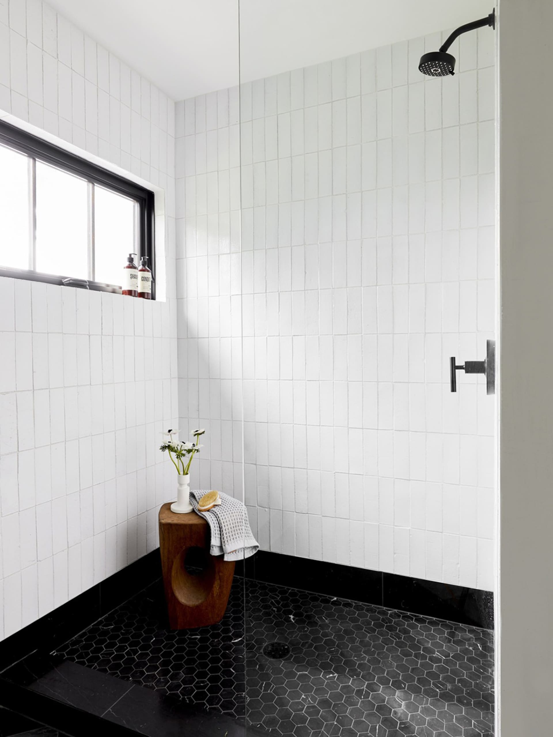 A modern bathroom with white tiled walls and black hexagonal floor tiles, featuring a shower stall.