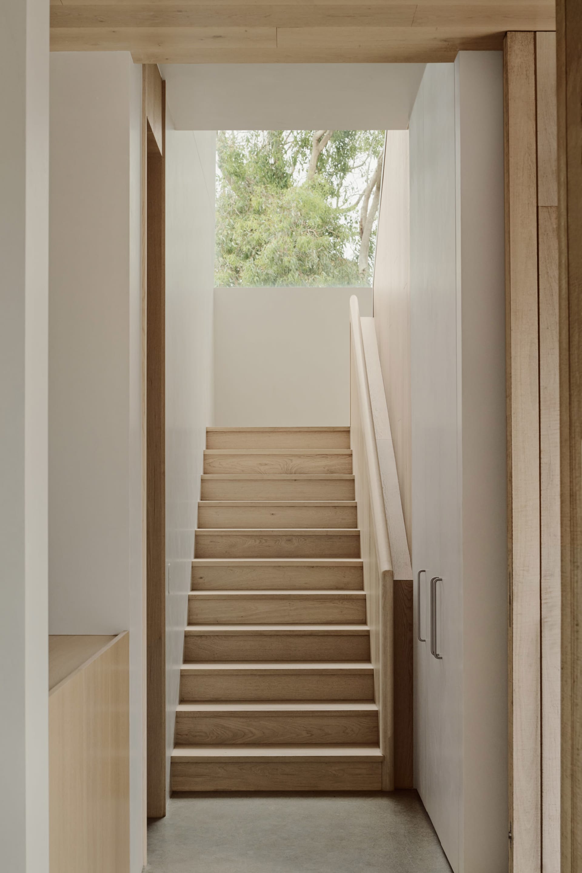 A minimalist staircase with wooden steps and handrail in a well-lit space.