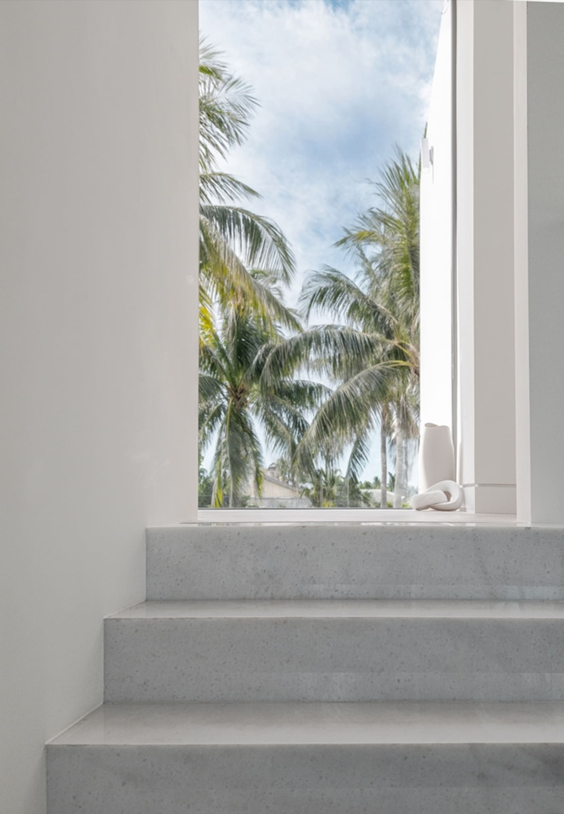 Modern interior space with concrete steps leading to an outdoor area with palm trees in the background.