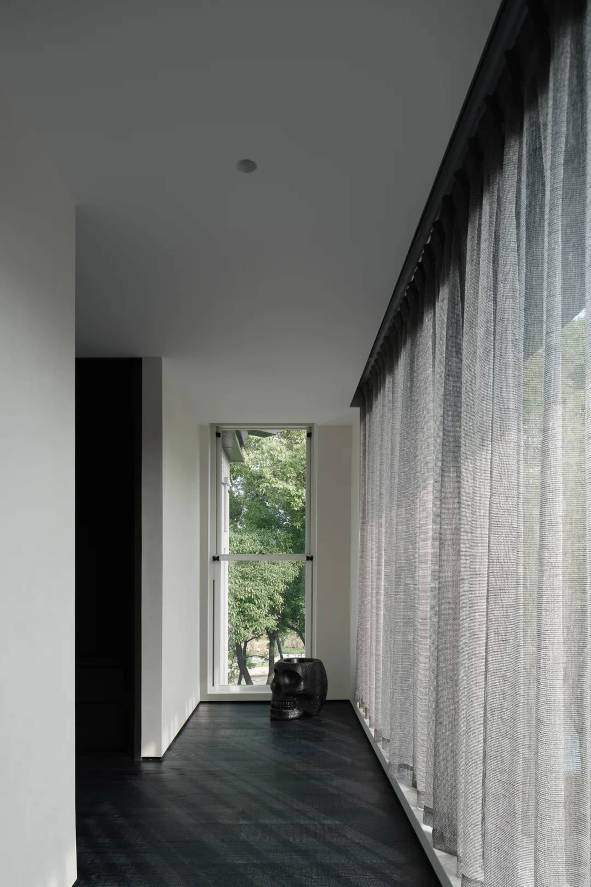 A minimalist bedroom featuring textured curtains and a dark floor, with a decorative skull on a table.