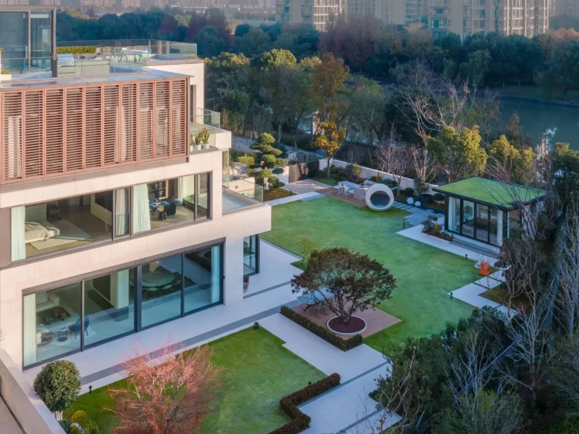 A modern house with a spacious outdoor garden featuring glass walls, concrete patio, and green lawn.
