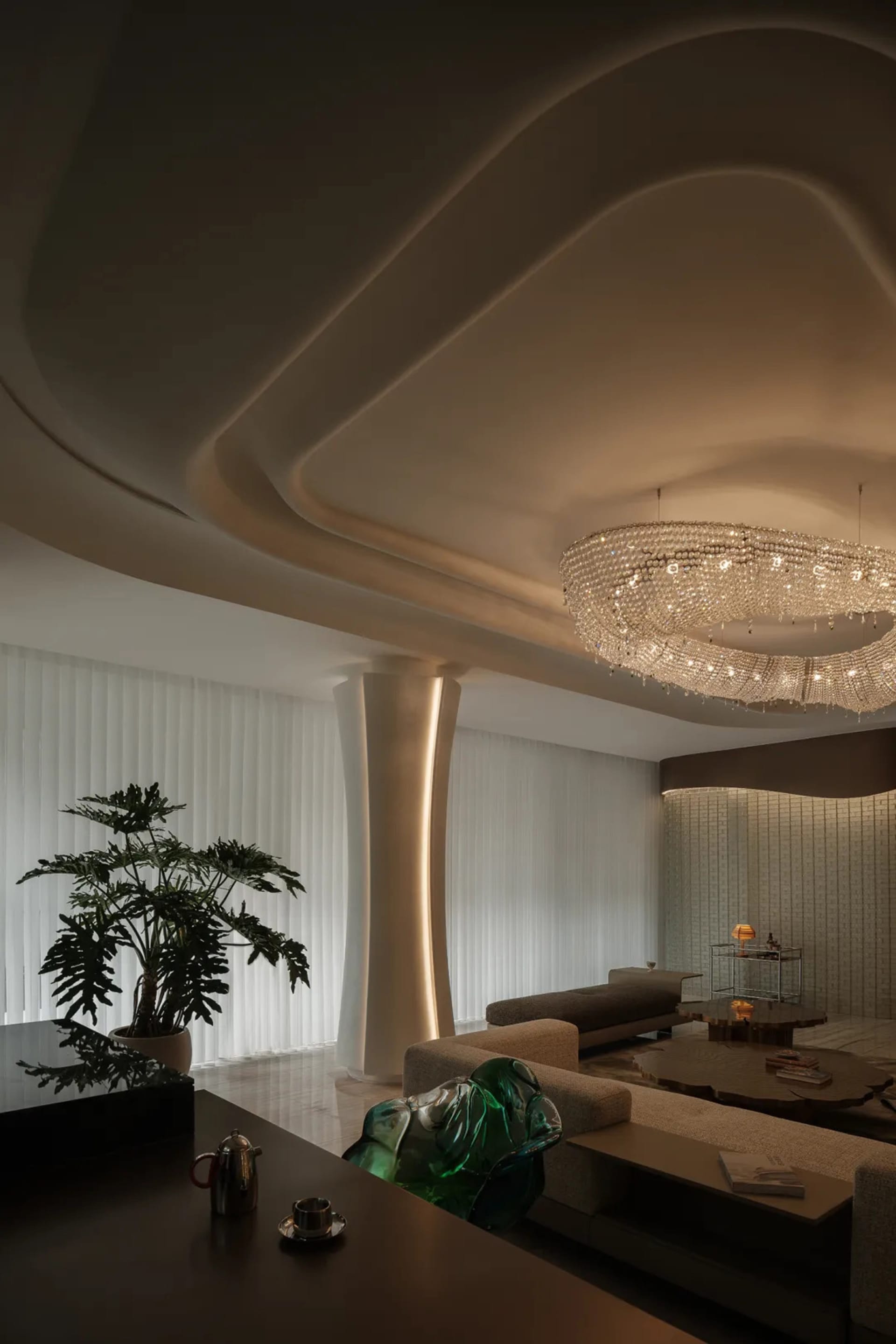 A modern living room with white textured walls and ceiling, featuring a chandelier, couches, and a potted plant.