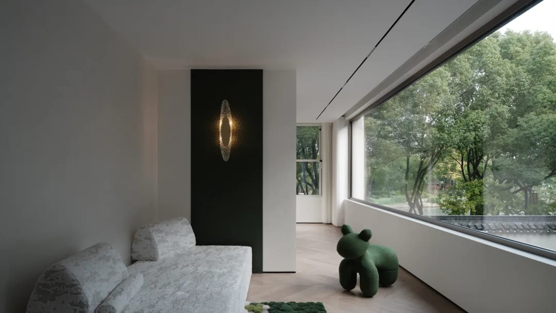 Contemporary minimalist living room featuring a sleek sofa, green animal-shaped ottoman, and a large window overlooking lush