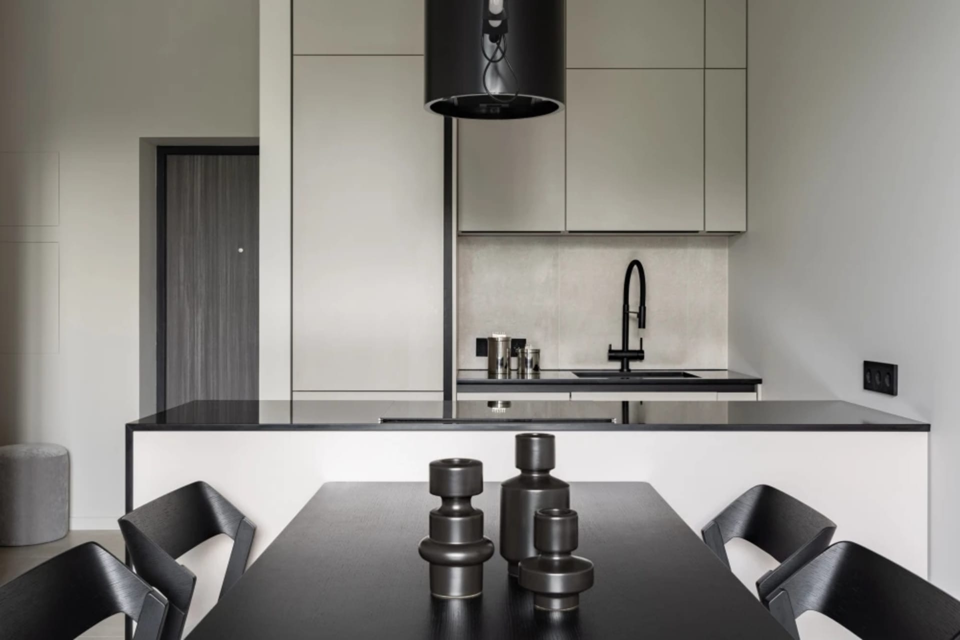 A modern, minimalist kitchen featuring black countertops, grey cabinets, and a glass backsplash.