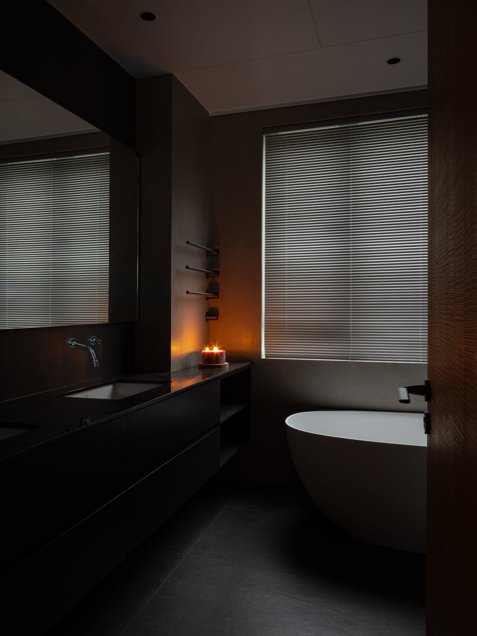 A modern bathroom with a concrete finish, featuring a freestanding bathtub, a floating vanity with a dark countertop, and a l