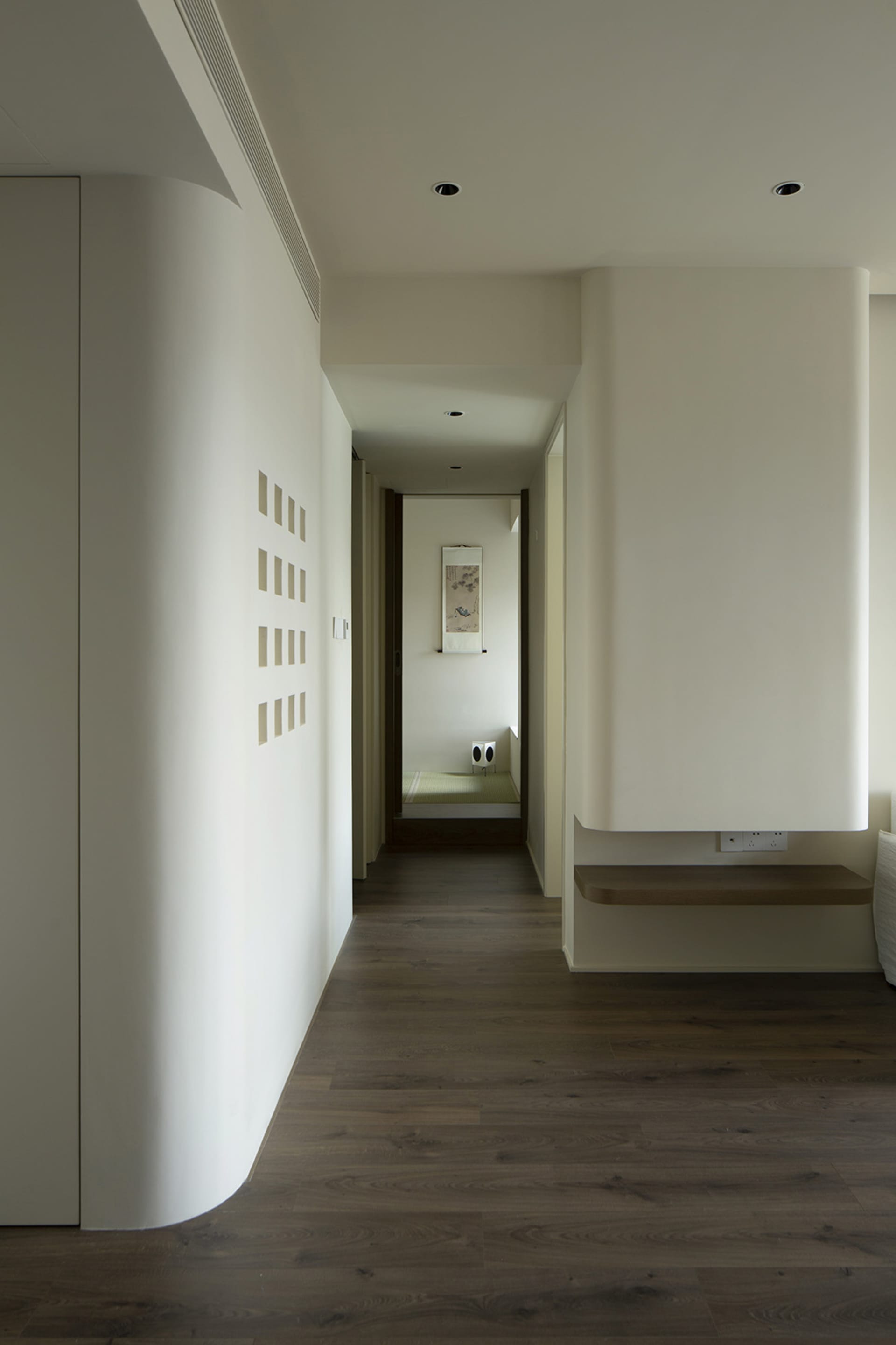 A modern, minimalist corridor with white walls and a wooden floor.