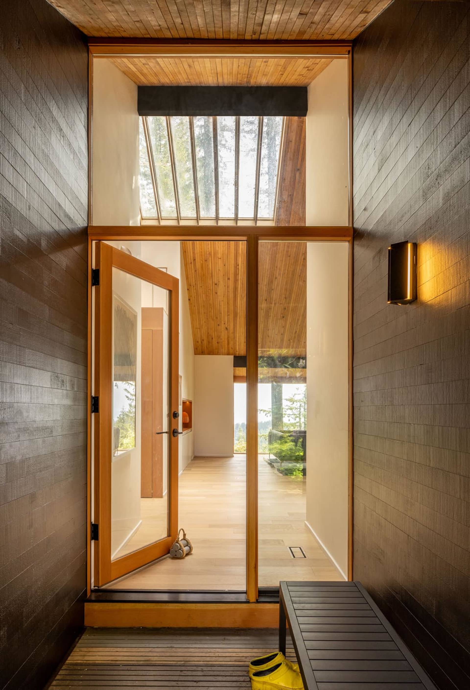 A modern entryway featuring wooden walls and a glass door with a skylight above.