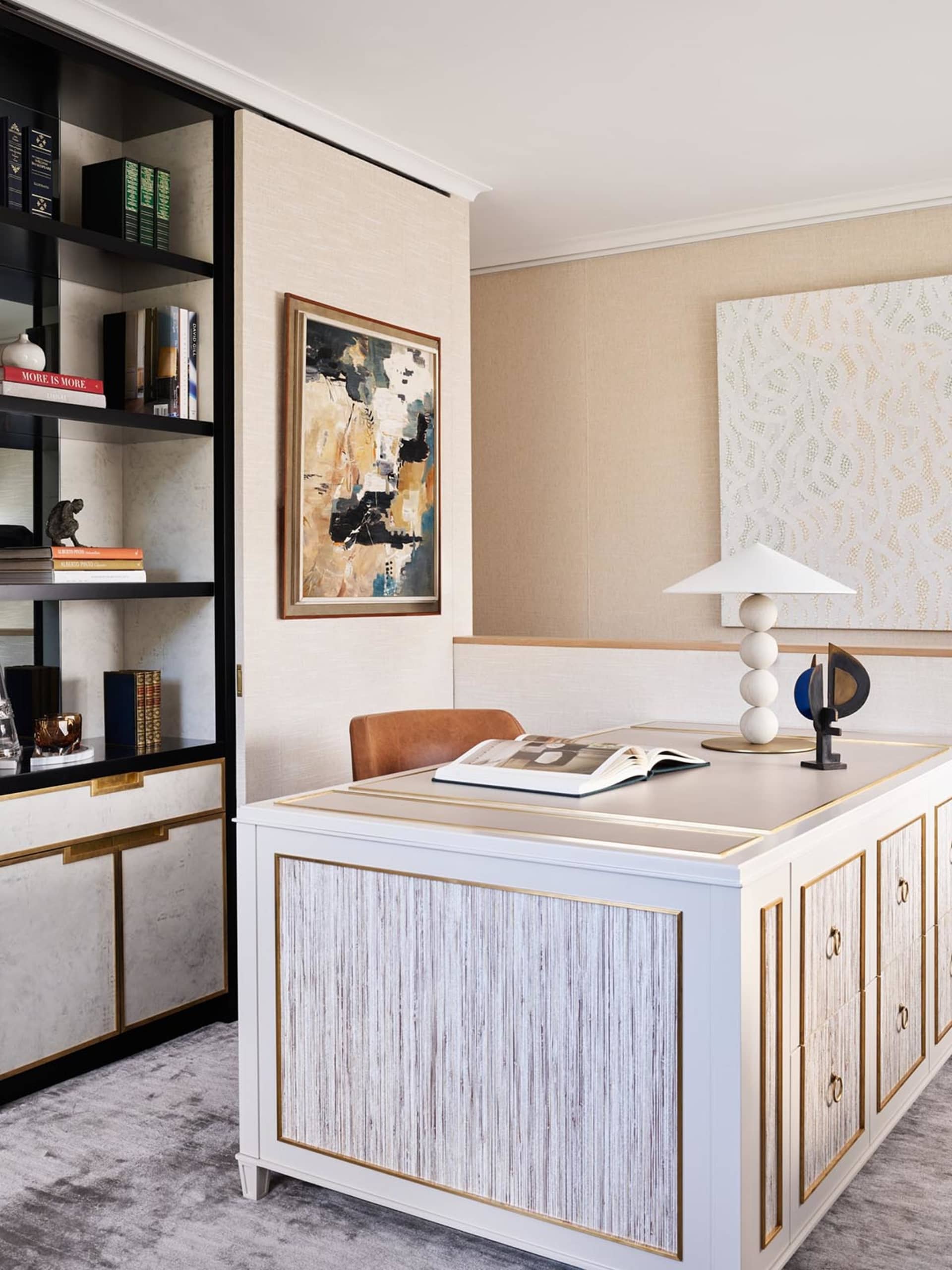 A modern home office featuring a white desk, abstract art, and leather chair.