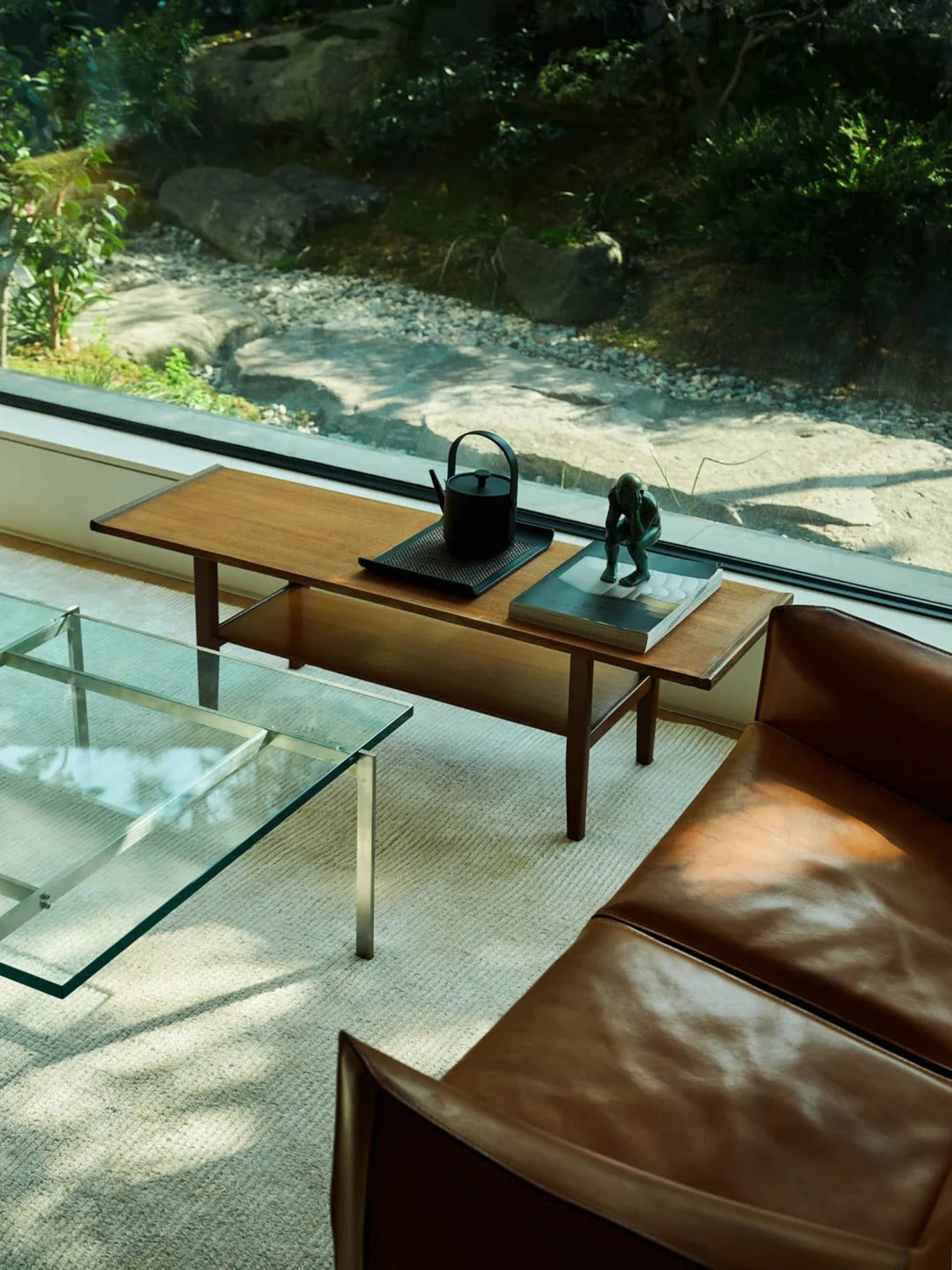 A modern interior design featuring a glass and wooden coffee table, a leather couch, and a natural stone wall with greenery o